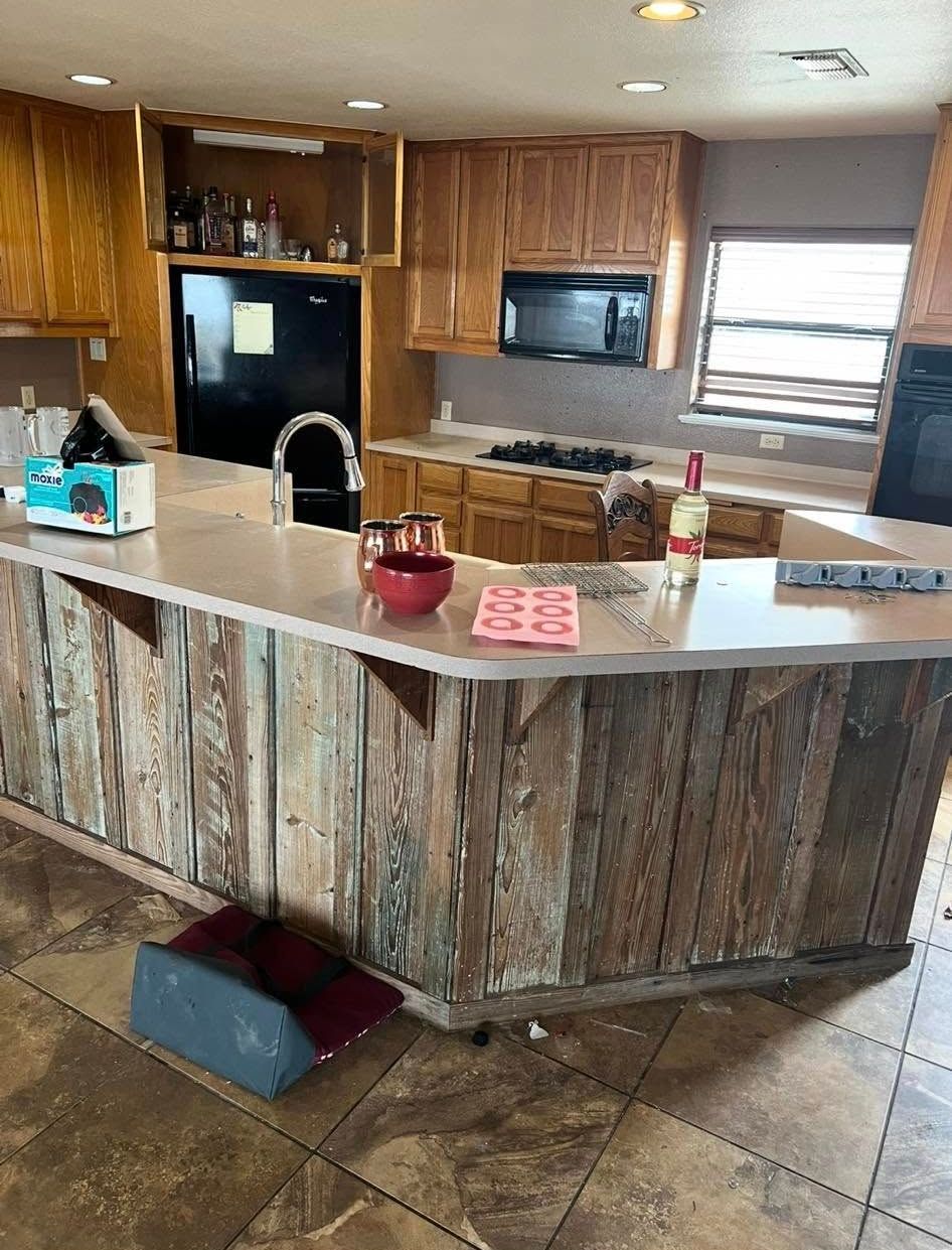 Kitchen with a rustic wooden island, light-colored countertops, and wooden cabinets. 