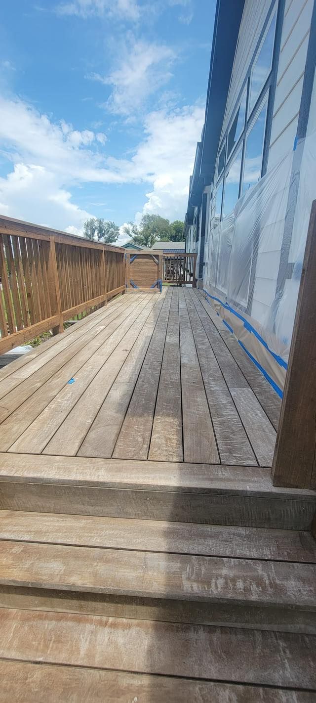 A weathered wooden deck with a wooden fence and a house on the right side, under a bright blue sky.