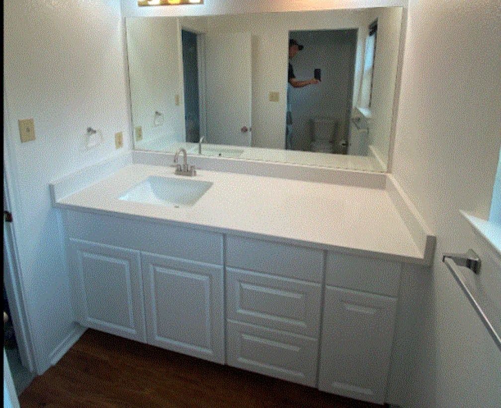 White bathroom vanity with a sink and a large mirror; a person is reflected in the mirror.