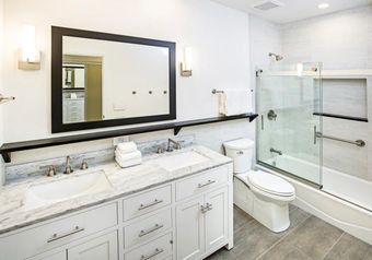 A white toilet sits against a light green wall in a bathroom with gray and white patterned floor tiles.