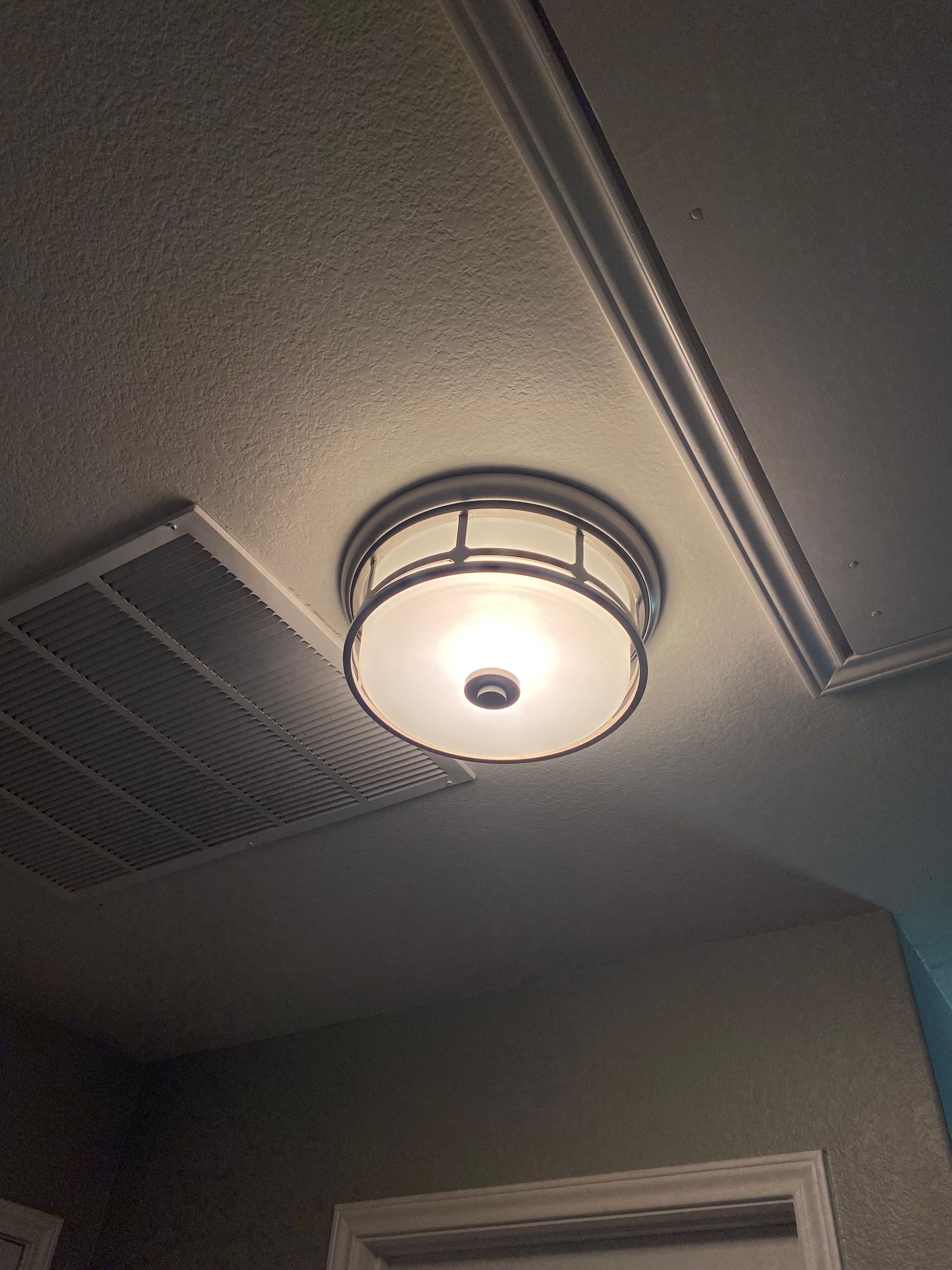 A ceiling light fixture with a frosted glass shade. It is centered in a room with an air vent and trim visible.