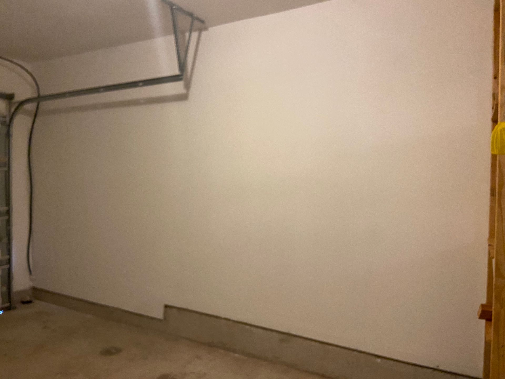 Interior view of a garage with a white wall, concrete floor, and the garage door mechanism visible at the top.