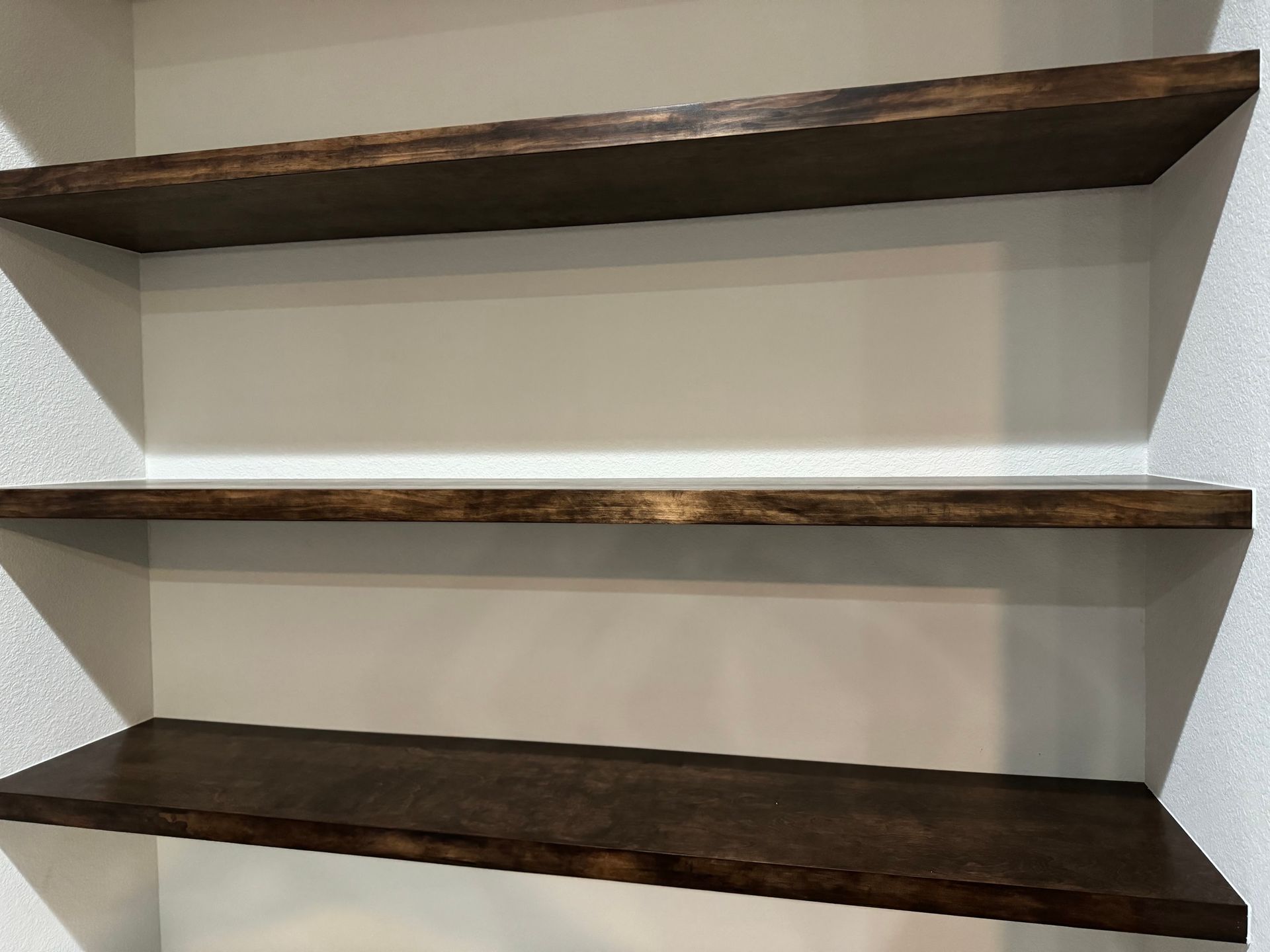 Three dark brown wooden shelves mounted on a beige wall.