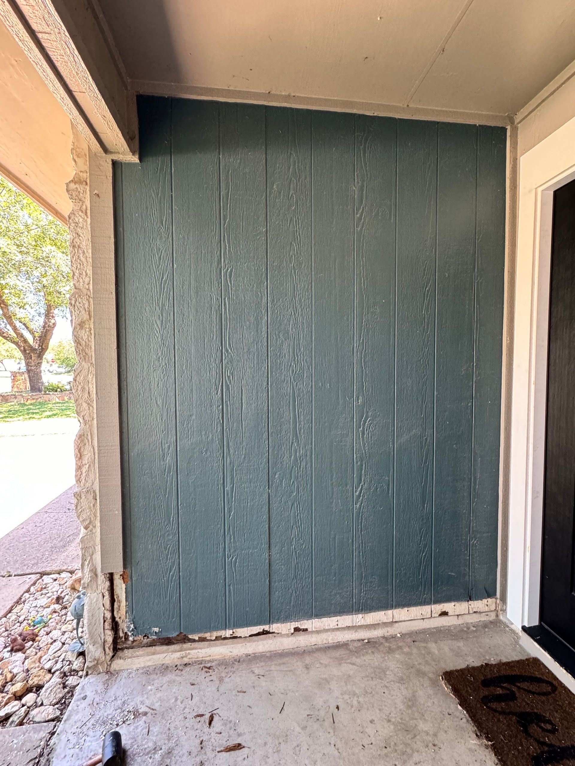 Blue wooden paneling on an exterior wall of a home's entry. Beige concrete and trim.