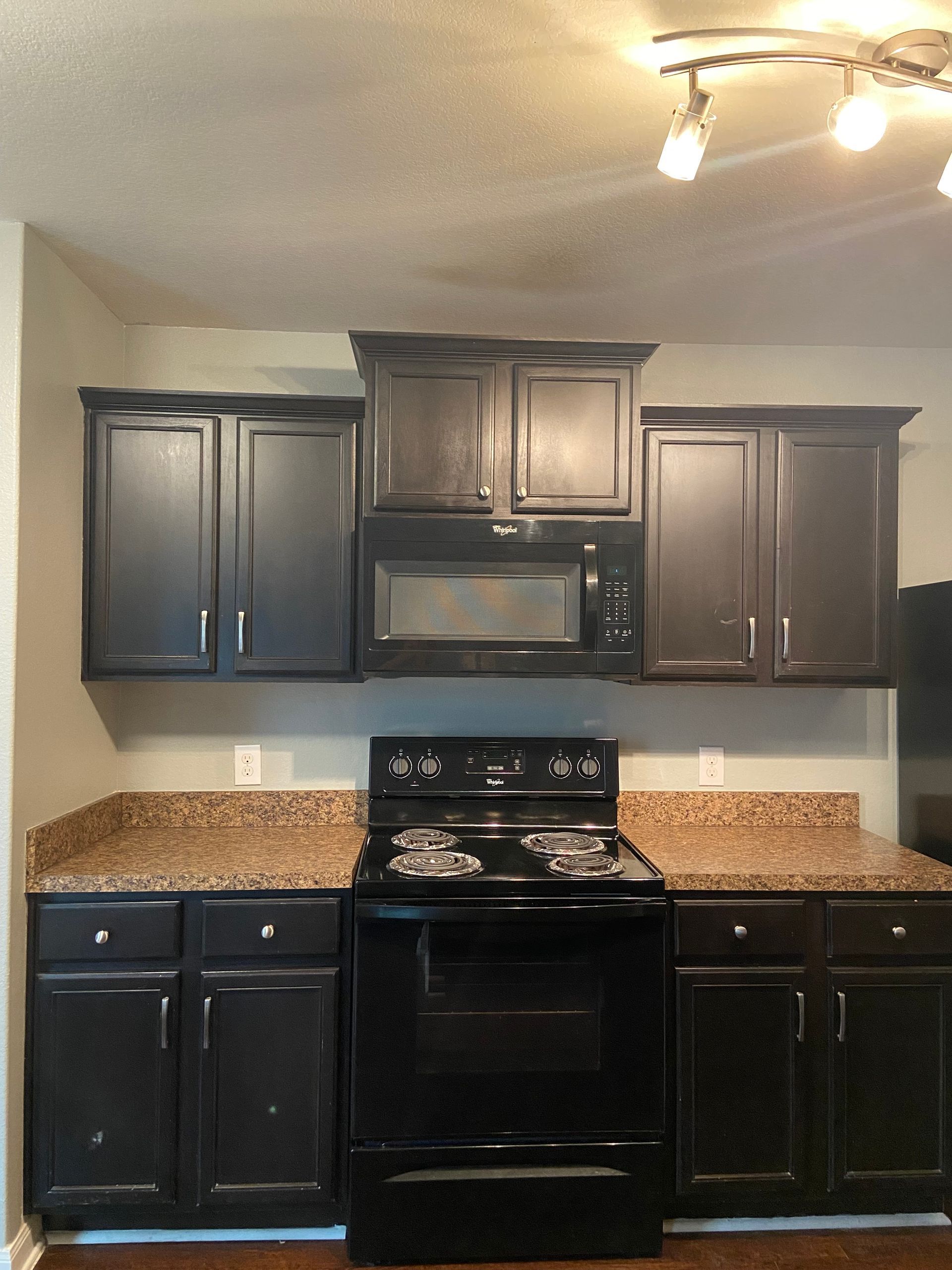 Black kitchen cabinets and appliances with tan countertops. A microwave sits above the stove.
