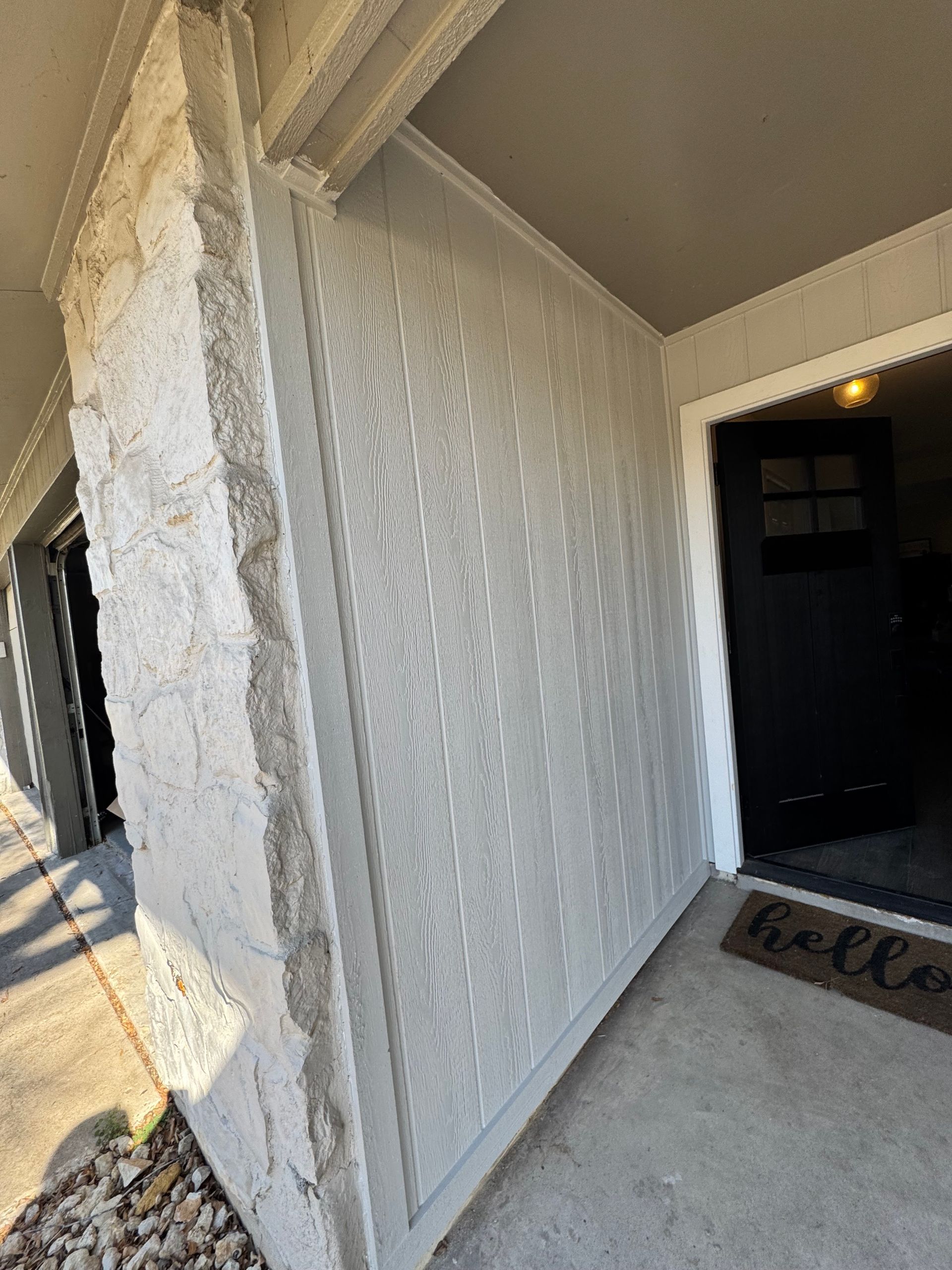 Exterior of a building with a textured, light-colored wall and a black door with a 