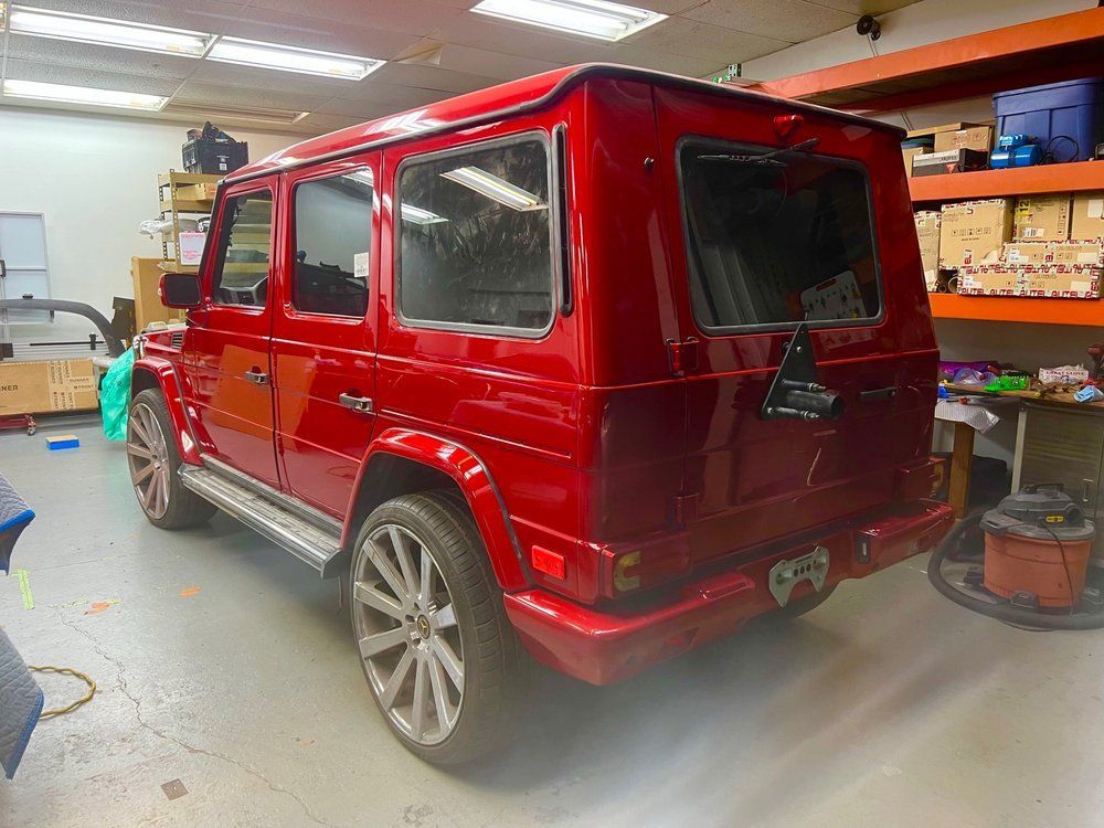 Red Mercedes-Benz G-Class SUV with silver wheels parked inside a shop with shelves.