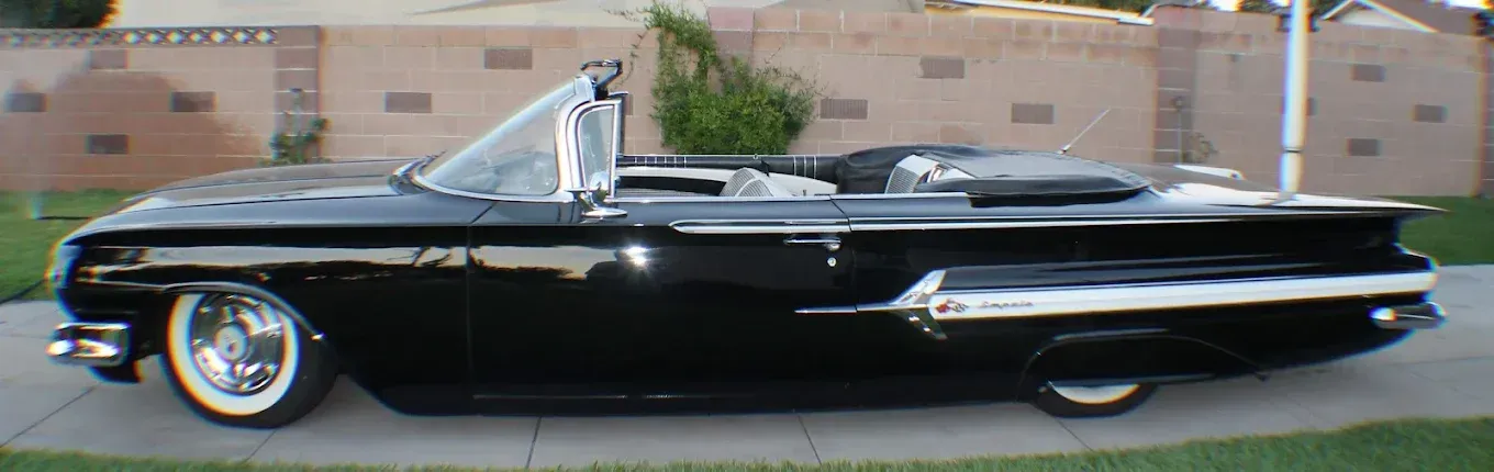 Black convertible car with white trim, parked on a driveway.