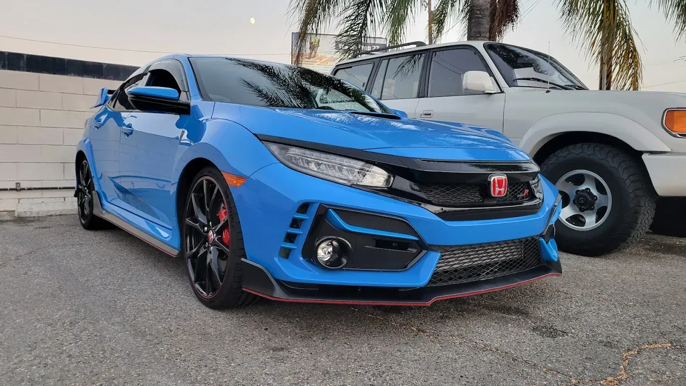 Blue Honda Civic Type R sports car parked next to a white SUV.