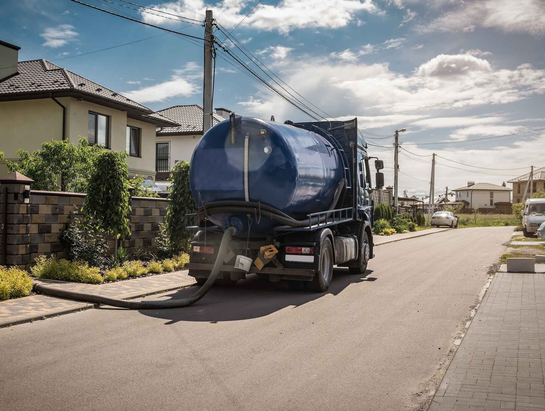 A septic tank truck is driving down a street in a residential area.