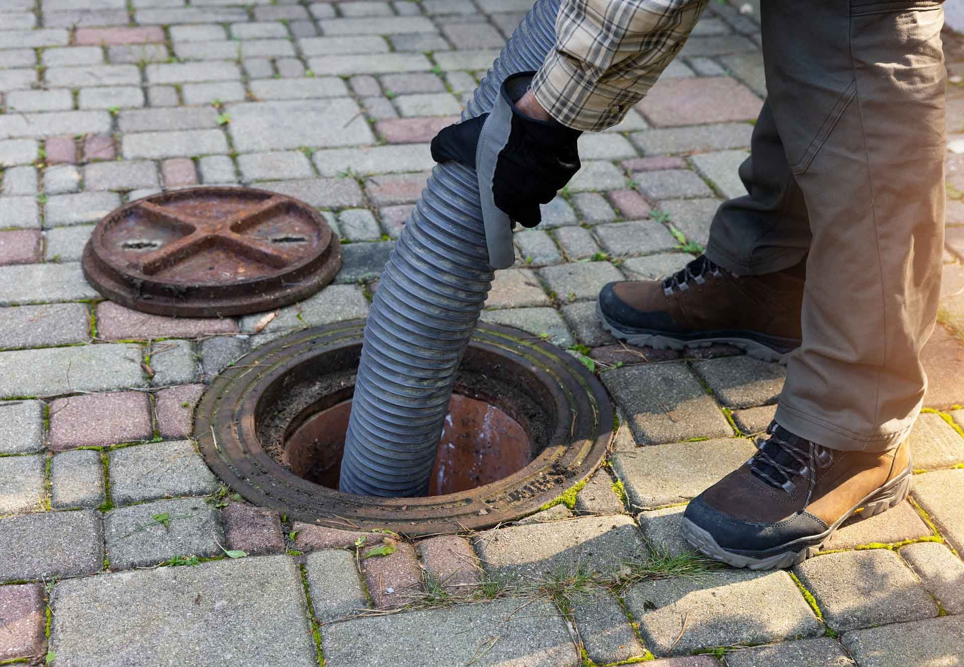 A man is pumping sewage into a manhole cover with a hose.