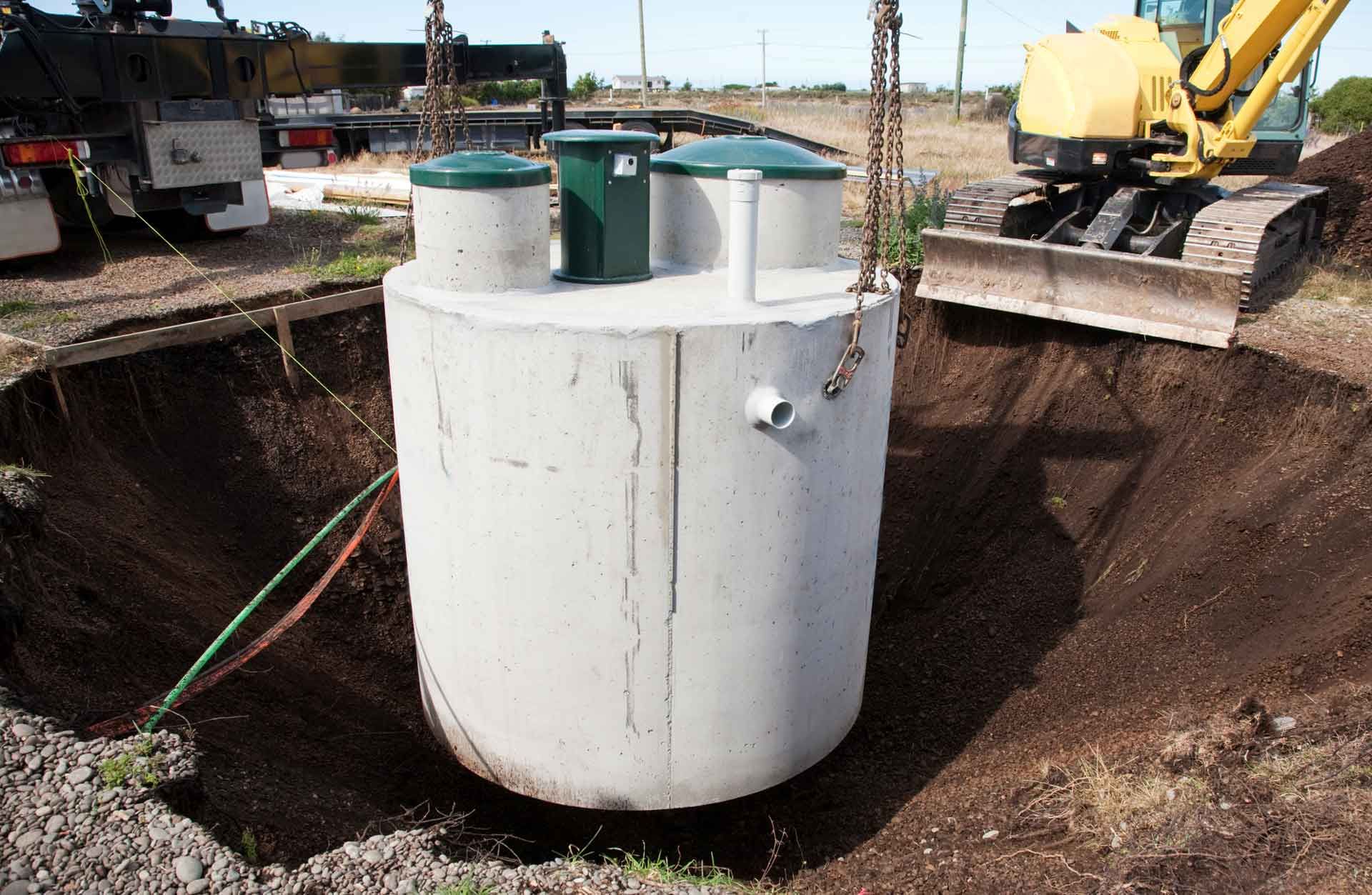 A large concrete tank is being lifted into a hole by a bulldozer