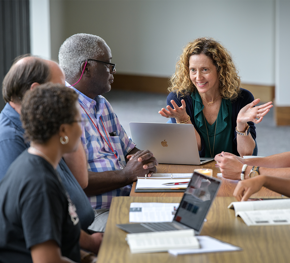 A group of people are sitting around a table with laptops.