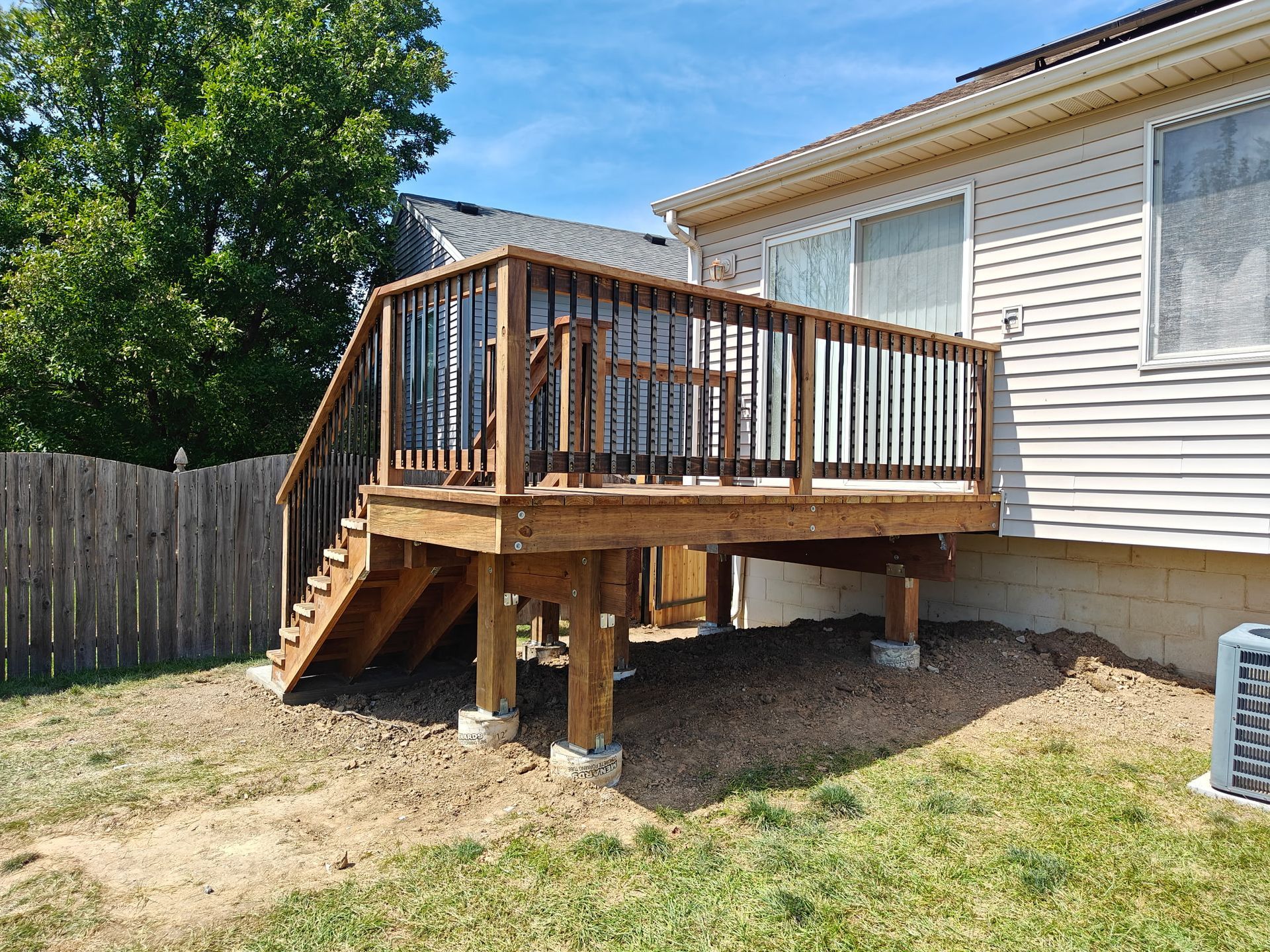 Wooden deck with stairs attached to a beige house, surrounded by a yard and a wooden fence.
