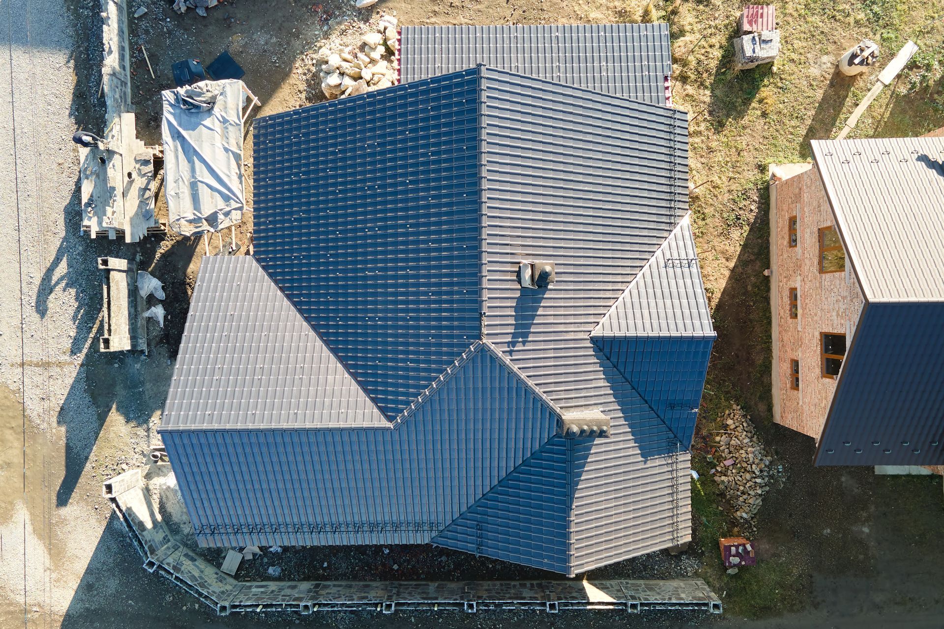 Overhead view of a house under construction with a dark blue shingled roof, construction materials nearby.