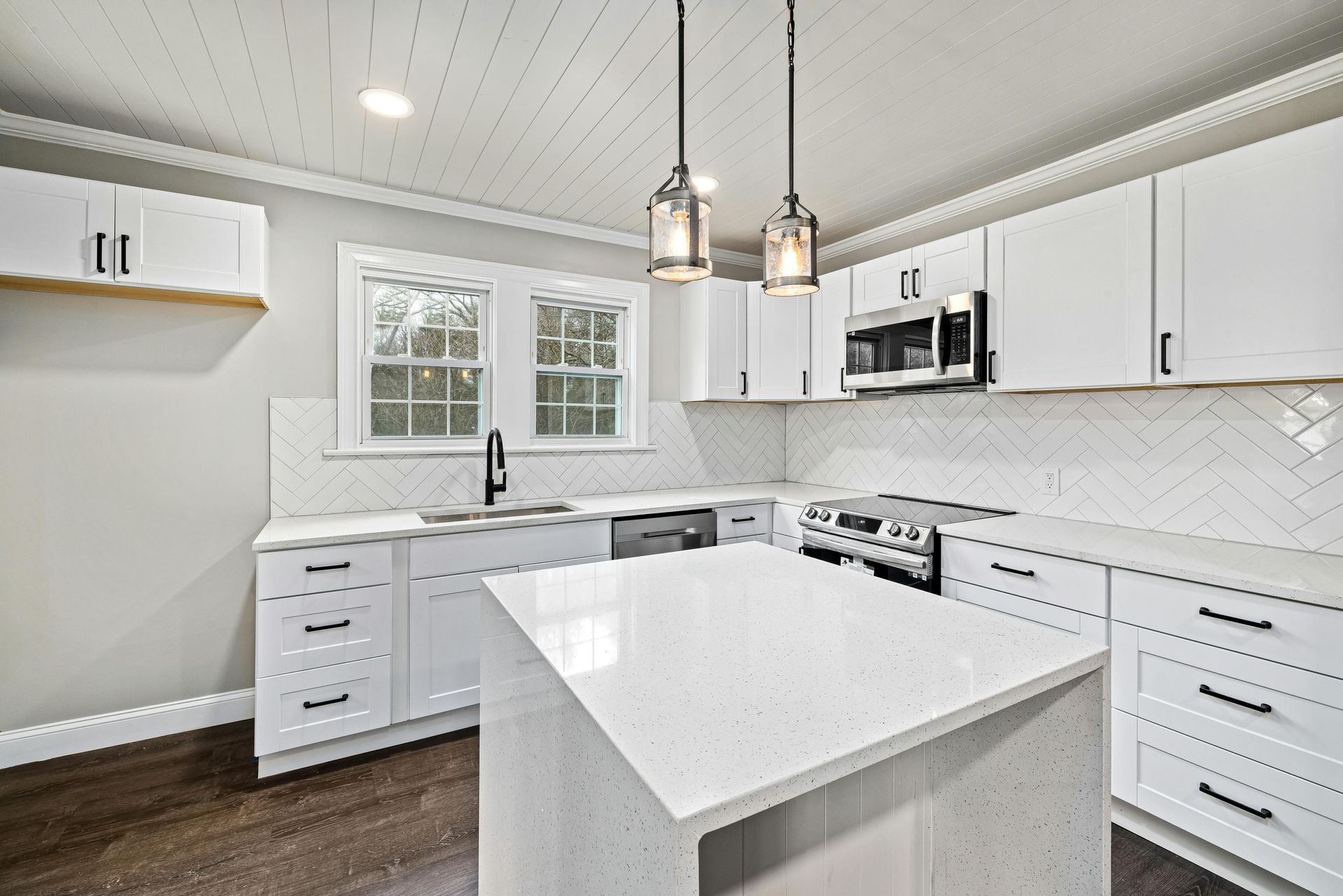 White kitchen with island, cabinets, and appliances. Beadboard ceiling, dark floors.