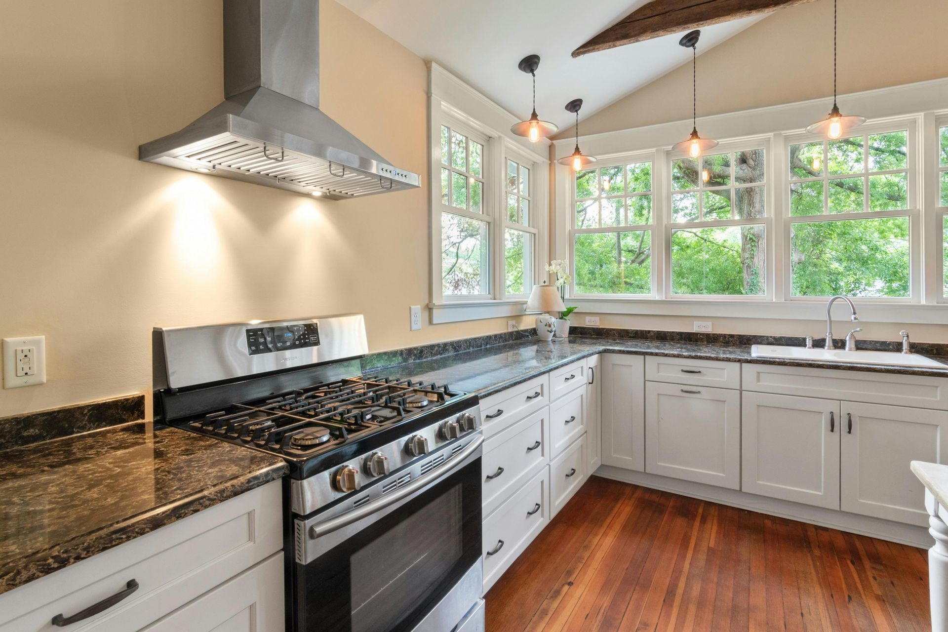 Modern kitchen with stove, range hood, white cabinets, granite countertops, and windows.
