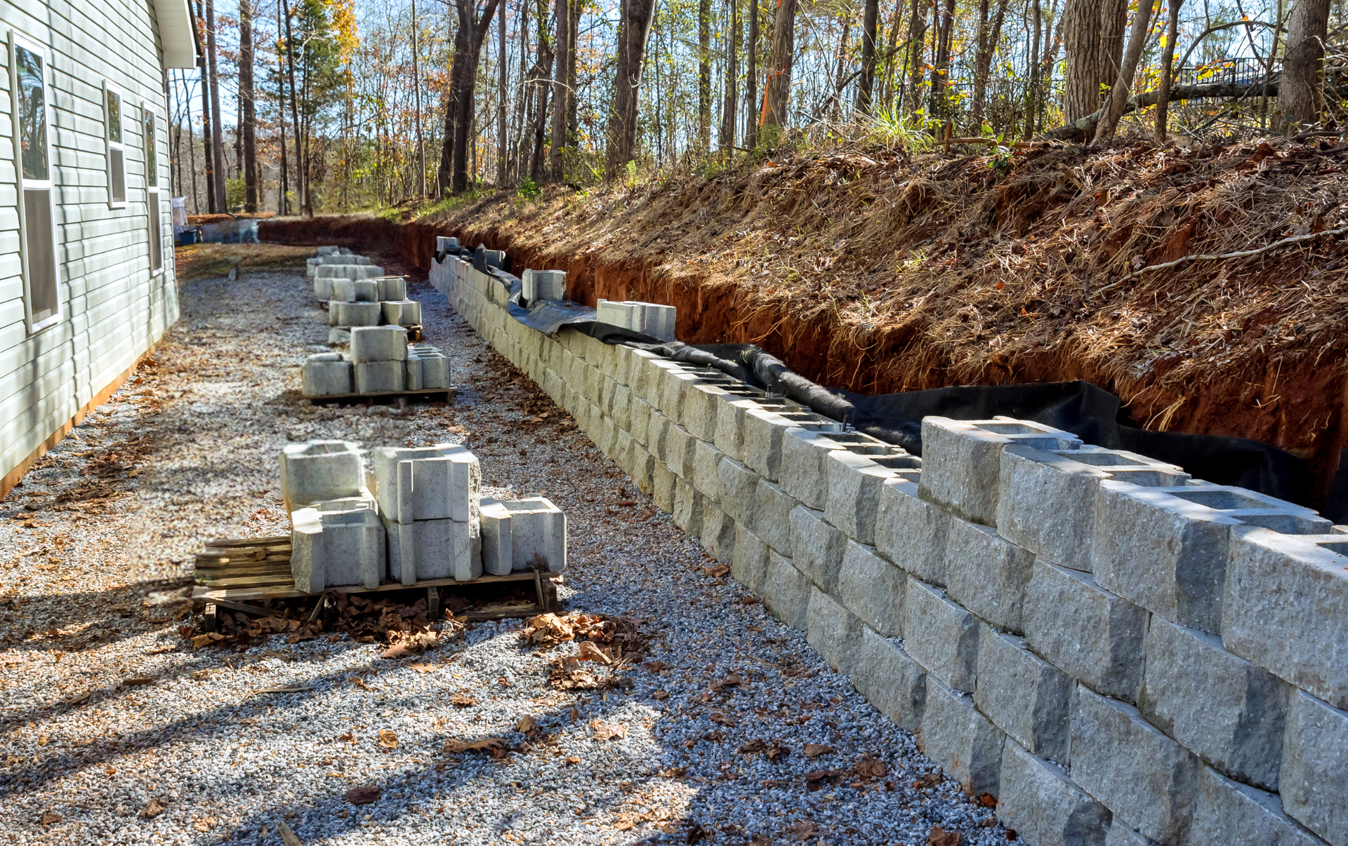 Retaining wall under construction with concrete blocks along a hillside next to a building.