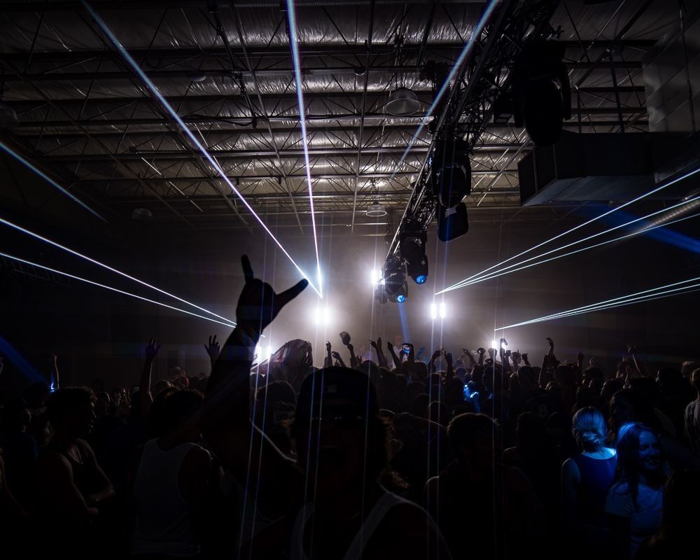 A crowd of people are standing in a dark room with their hands in the air.