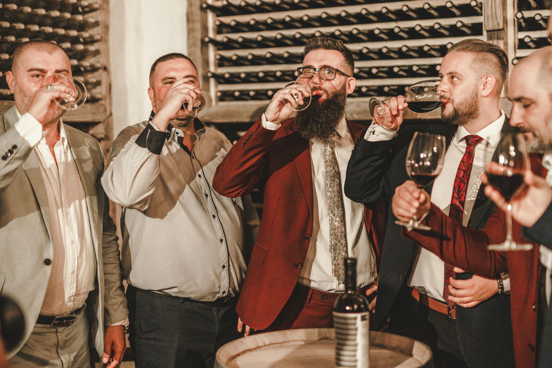 A group of men are drinking wine together in a wine cellar.
