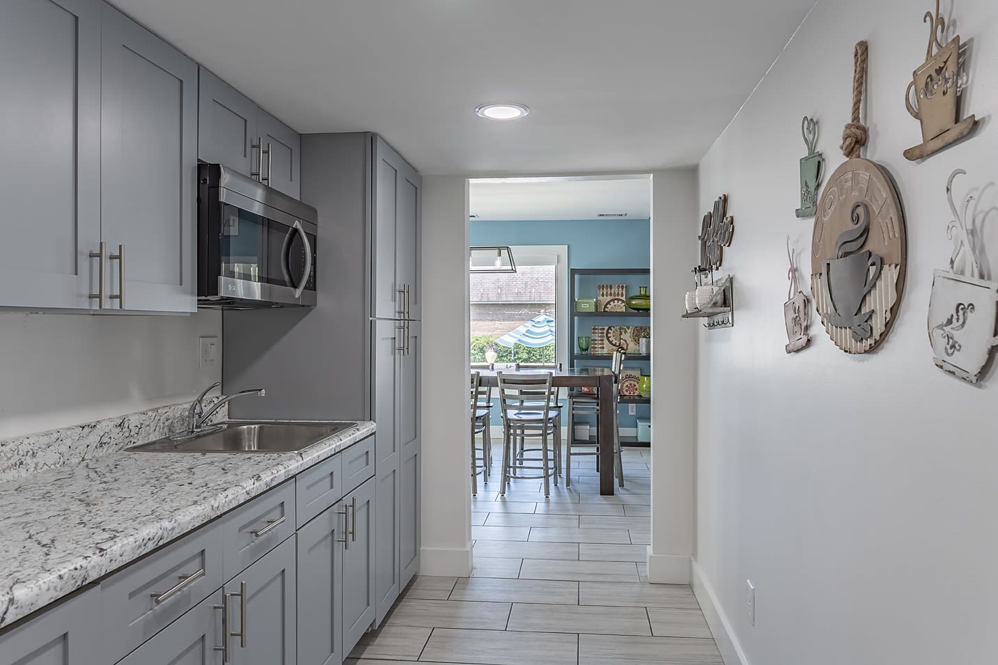 Galley kitchen with gray cabinets, granite countertops, stainless appliances, and a doorway to a blue dining area.