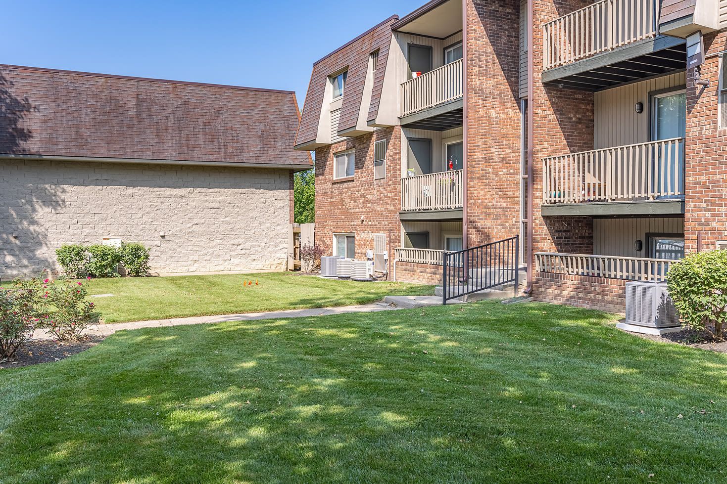 Exterior view of brick apartment building with balconies and a green lawn courtyard.