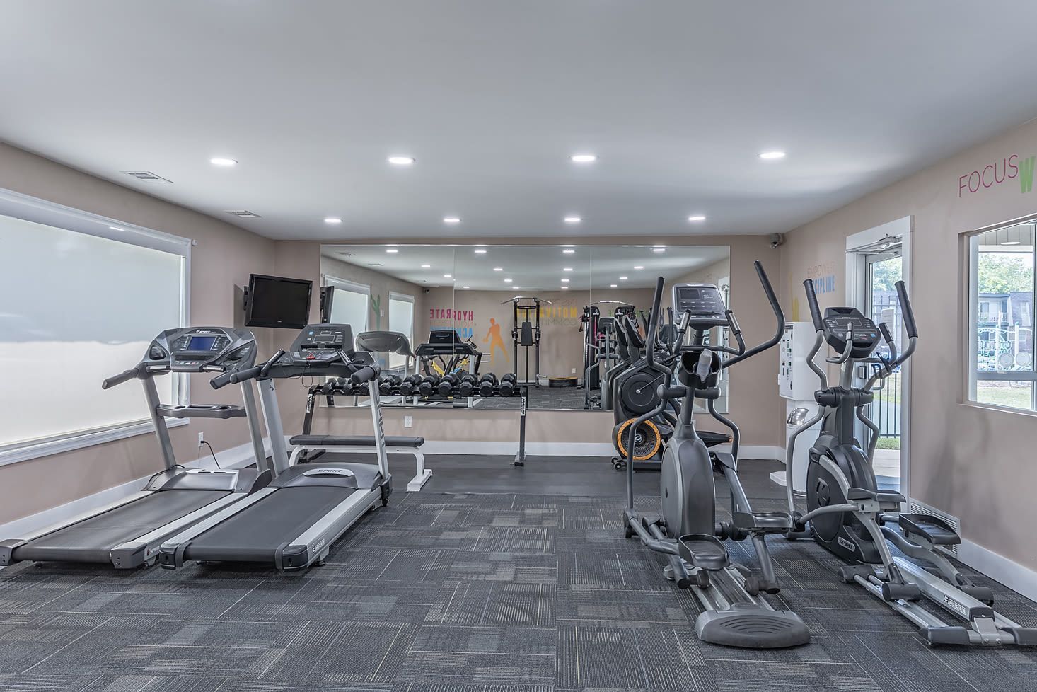 Indoor fitness center with treadmills, ellipticals, free weights, and a mirrored wall.