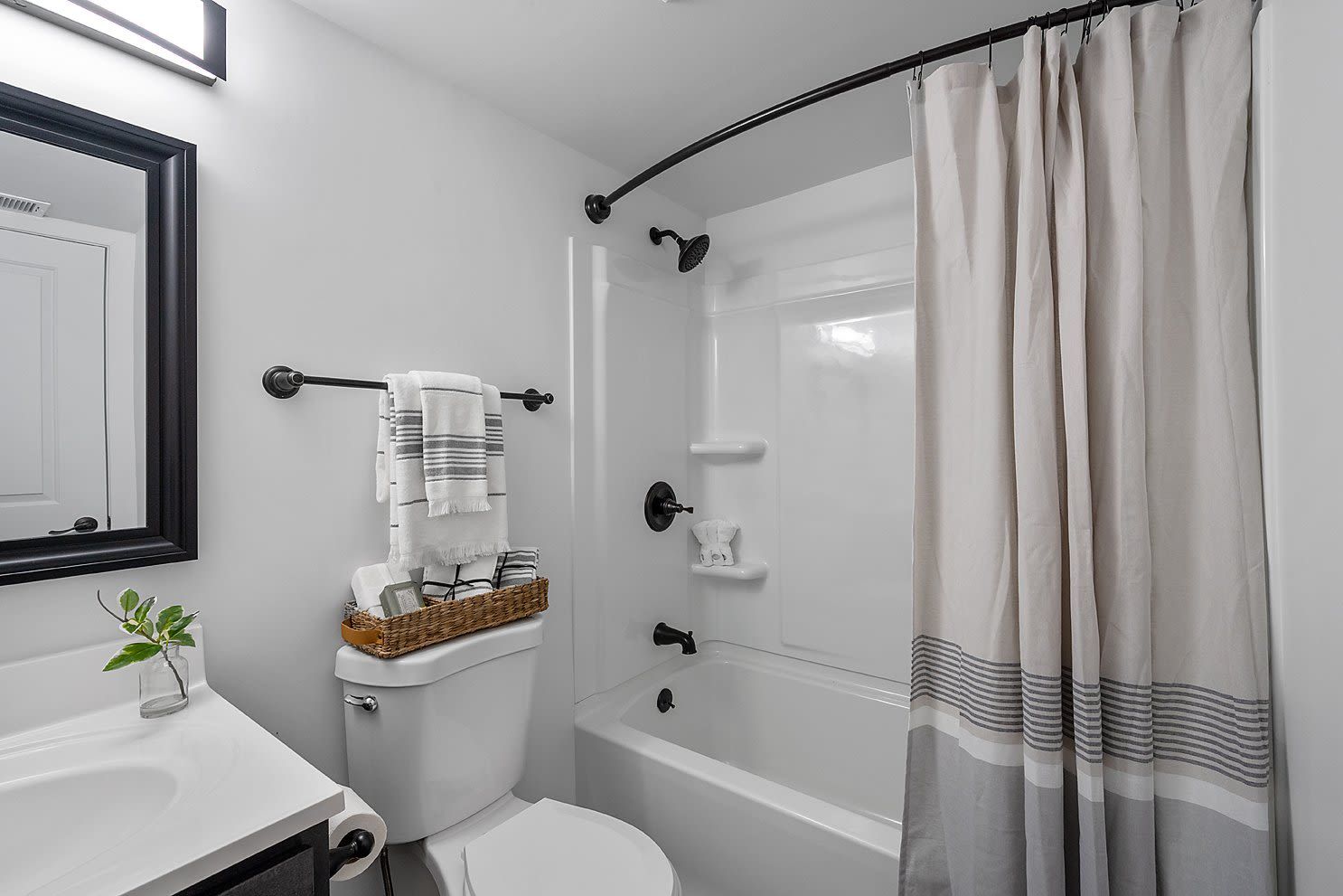 Bathroom with tub/shower, curved shower rod, white fixtures and sink.
