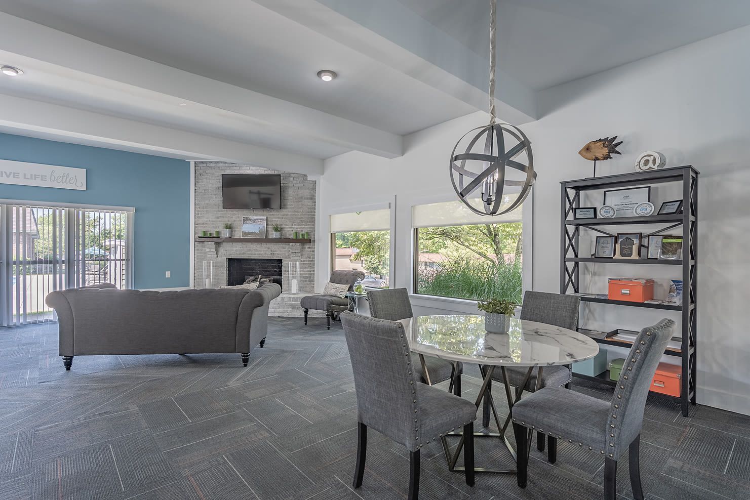 Modern community lounge with gray seating, a fireplace, TV, and round glass dining table.