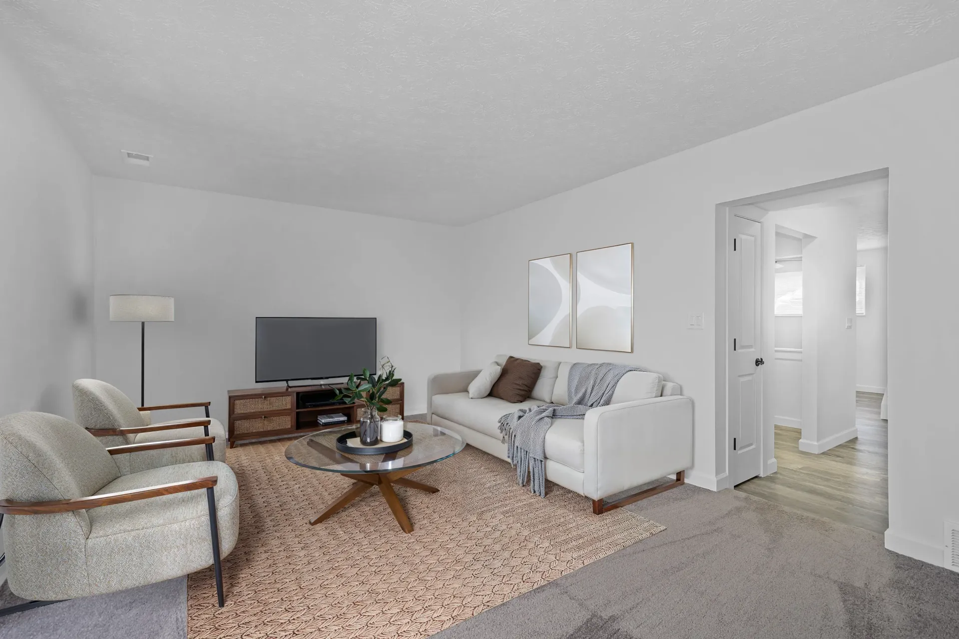 Living room in a modern apartment with sofa, two armchairs, a coffee table, and a hallway doorway.