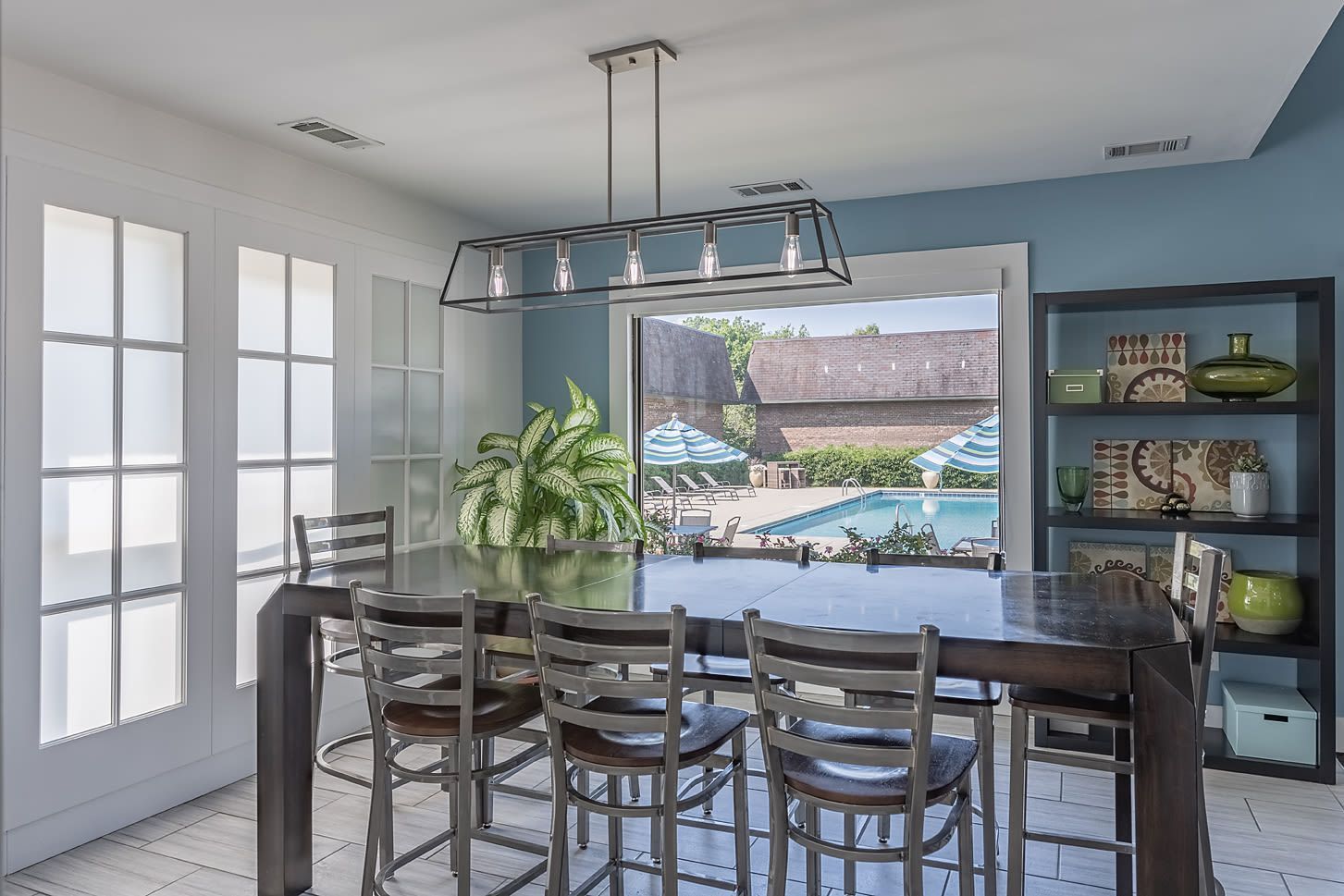 Dining area in a modern apartment with a dark wood table and metal chairs, pool visible through a large window.