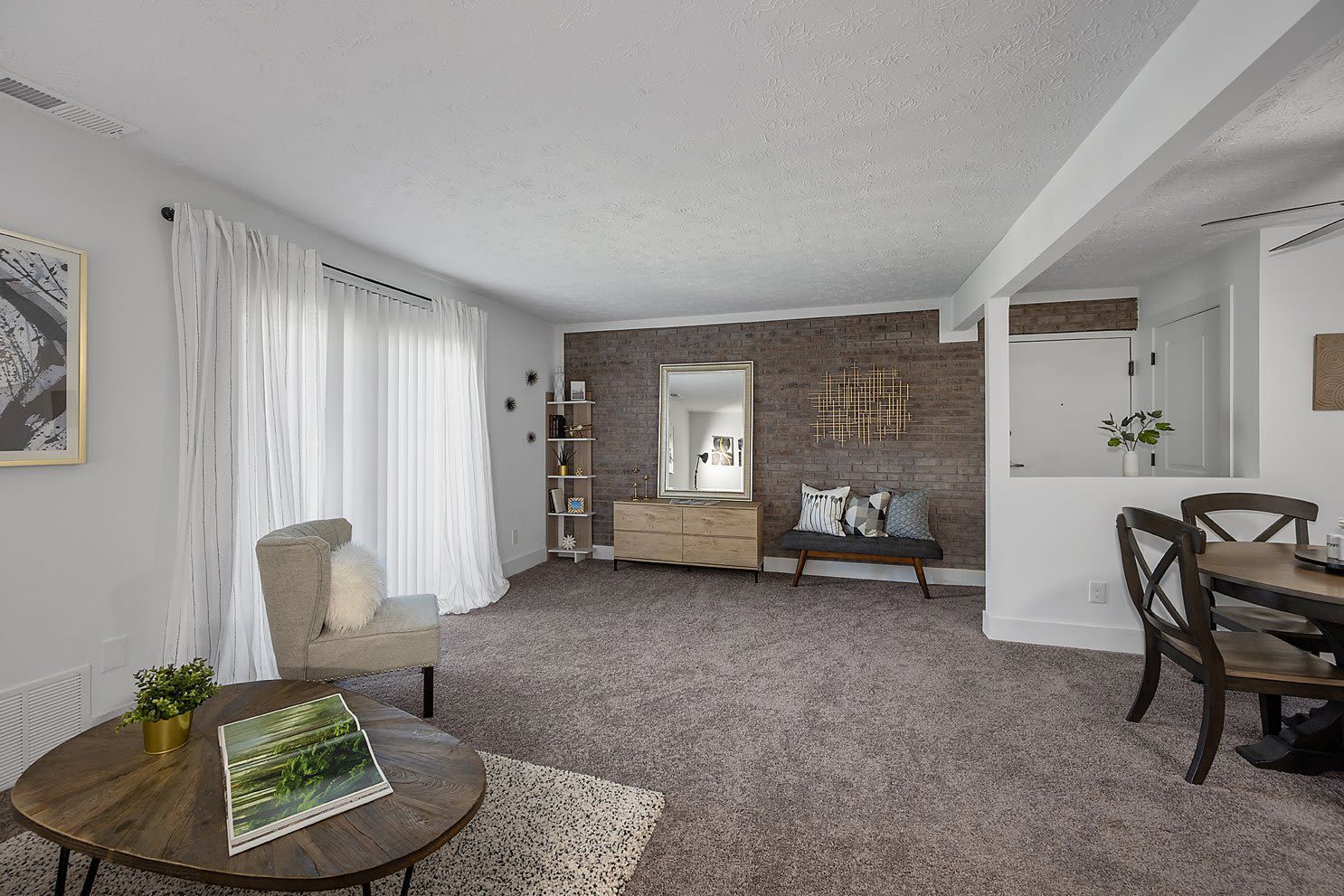 Living room with a brick accent wall, neutral furniture, and sheer white curtains.