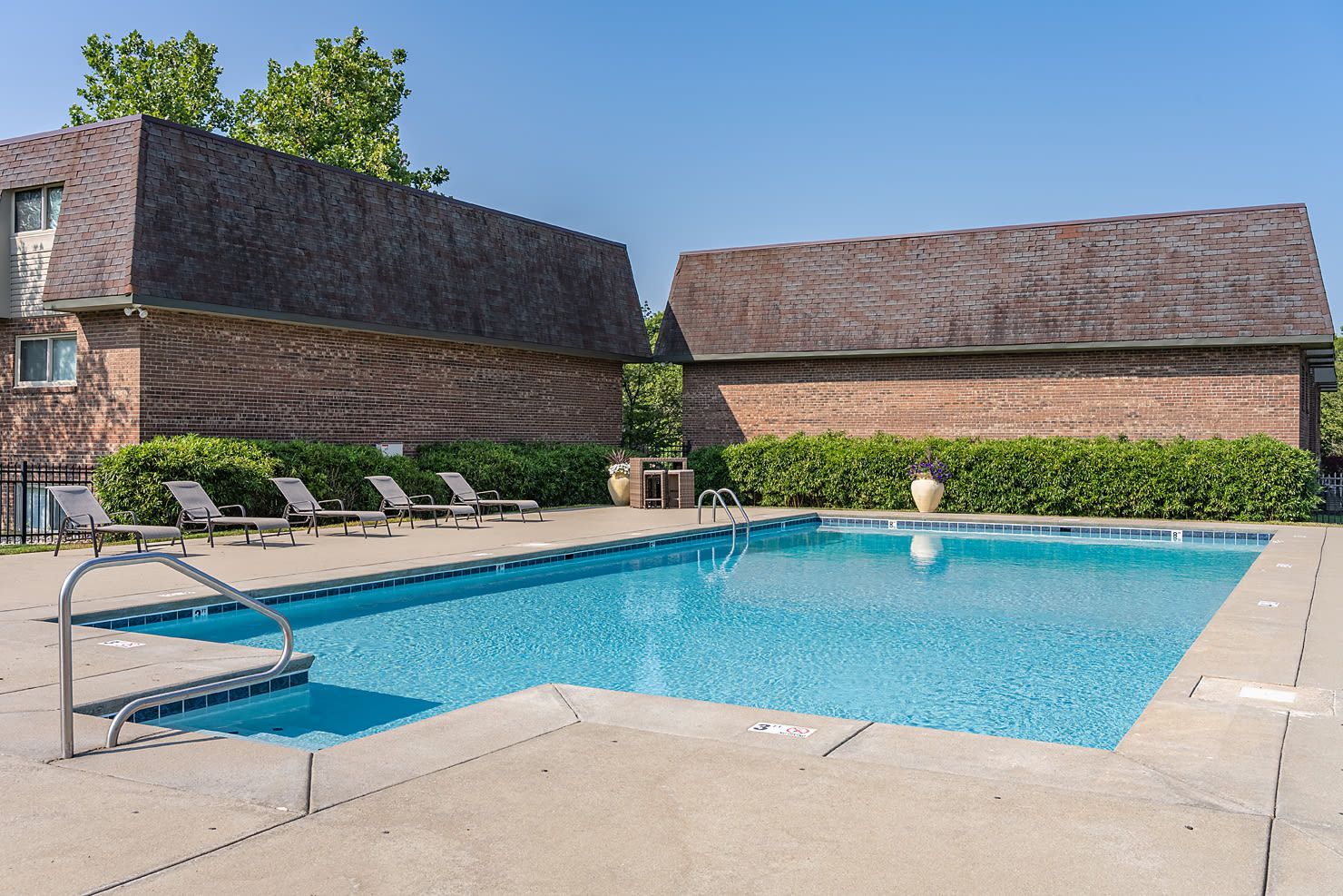 Outdoor community pool with lounge chairs and brick buildings in the background.