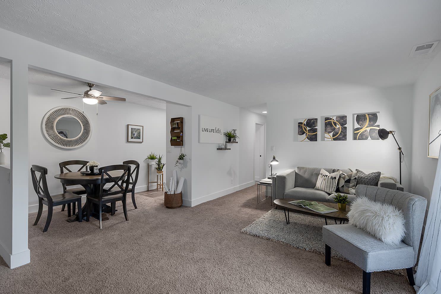 Open-concept living room and dining area in a modern apartment with a gray sofa, round dining table, and neutral decor.