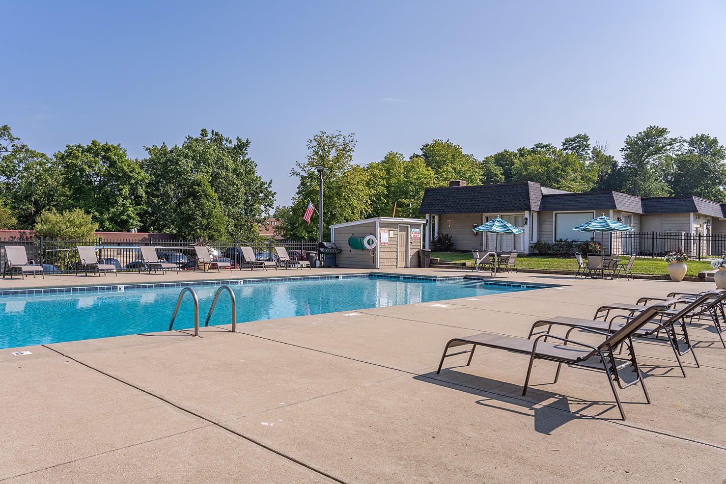 Outdoor pool at an apartment community with lounge chairs and striped umbrellas.