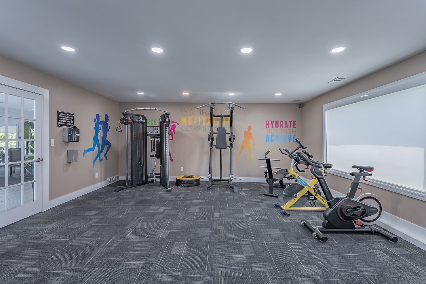 Well-lit community gym with weight machines, cardio bikes, and wall graphics.