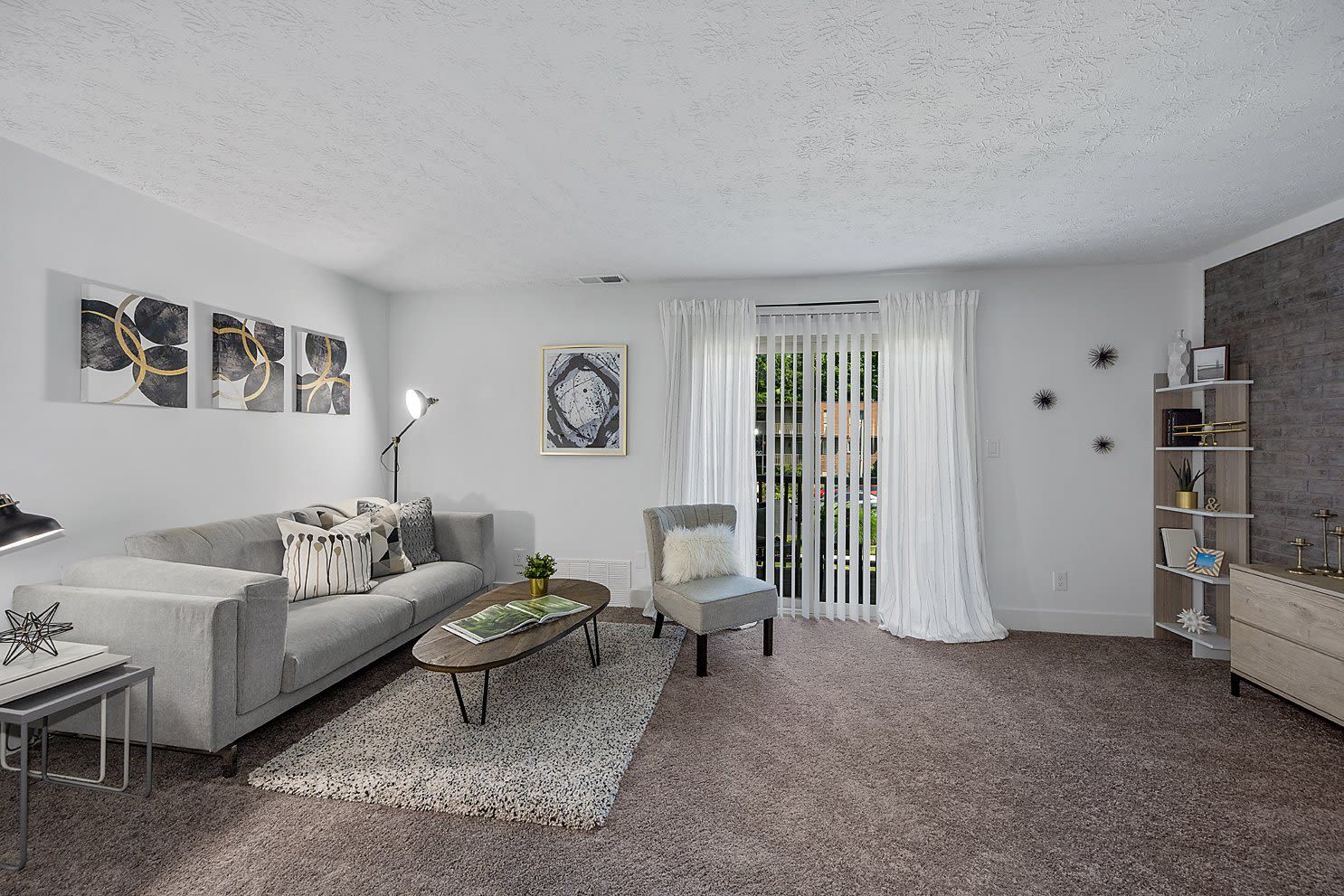 Living room in a modern apartment with a gray sofa, chair, and a balcony door.