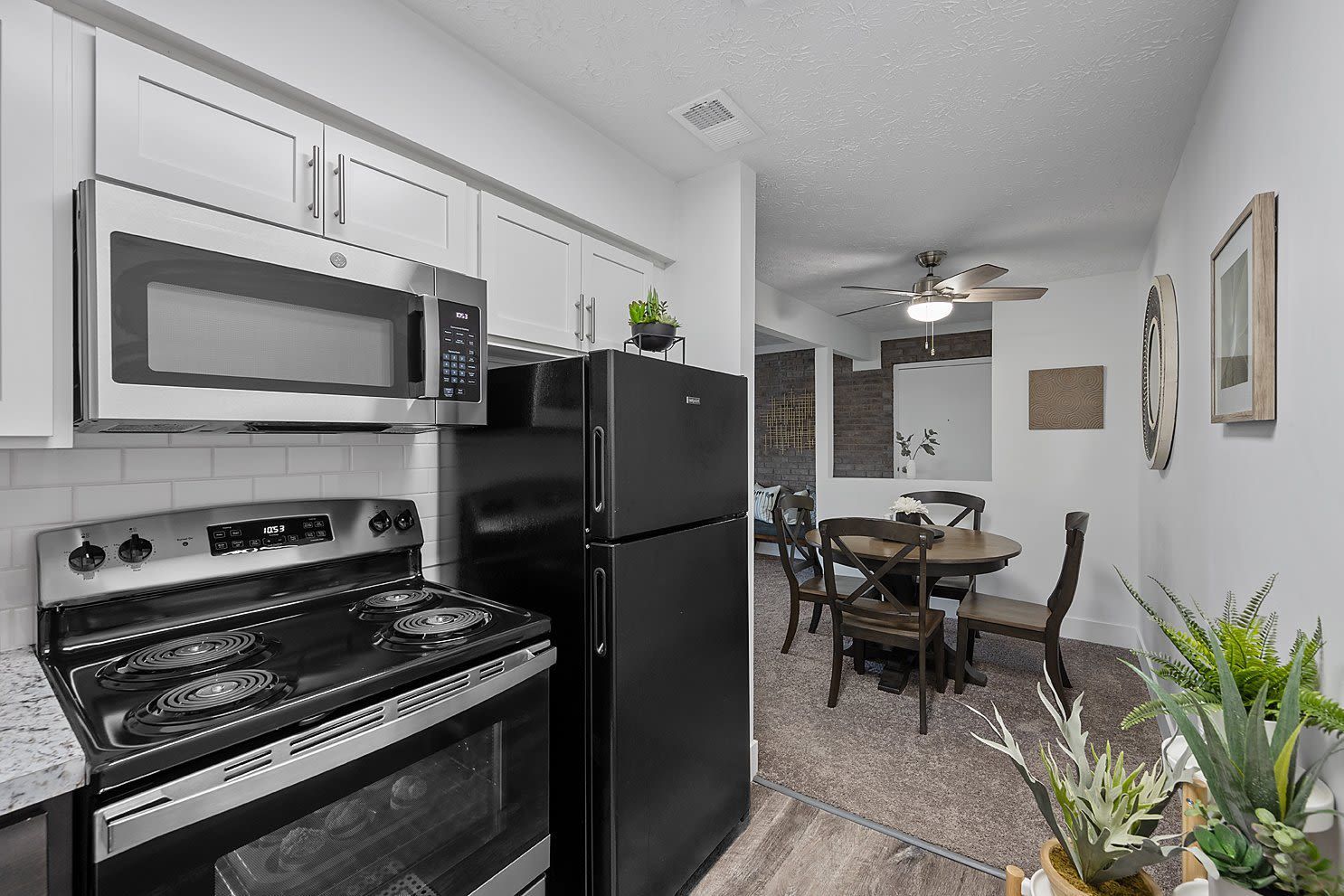 Kitchen in a modern apartment: white cabinets, black refrigerator and stove, adjacent dining area.