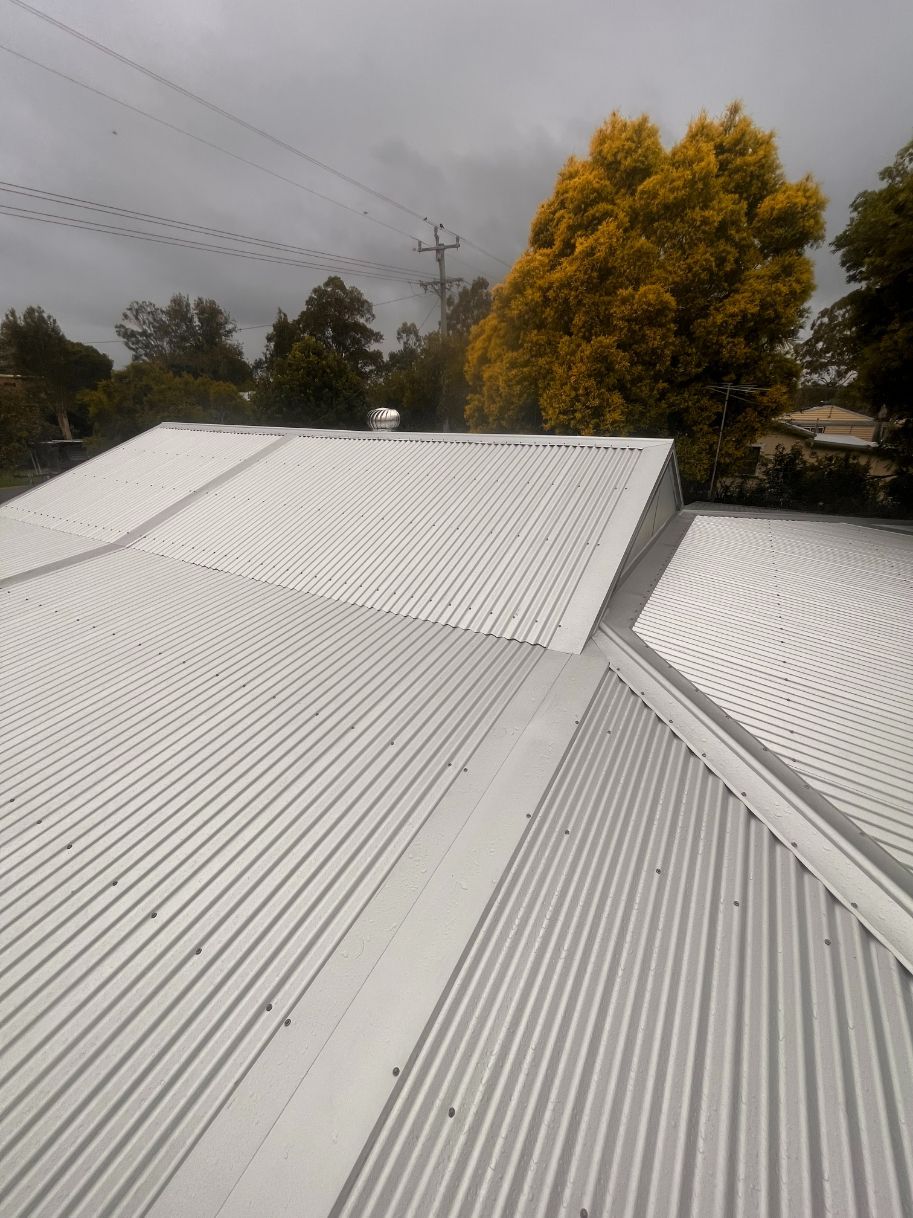 A White Corrugated Metal Roof With a Yellow Tree in the Background — Eli Mcauley Constructions in Grafton, NSW