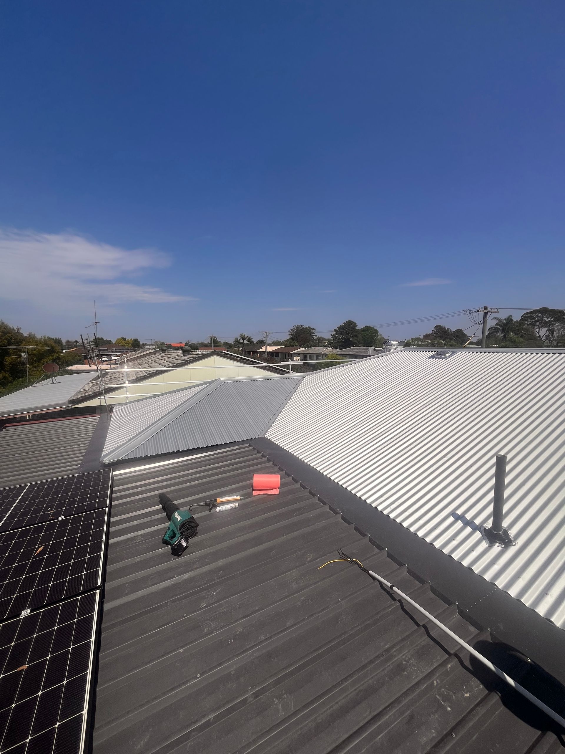 View of rooftops, solar panels, and construction tools on a sunny day. Blue sky, buildings in the background.