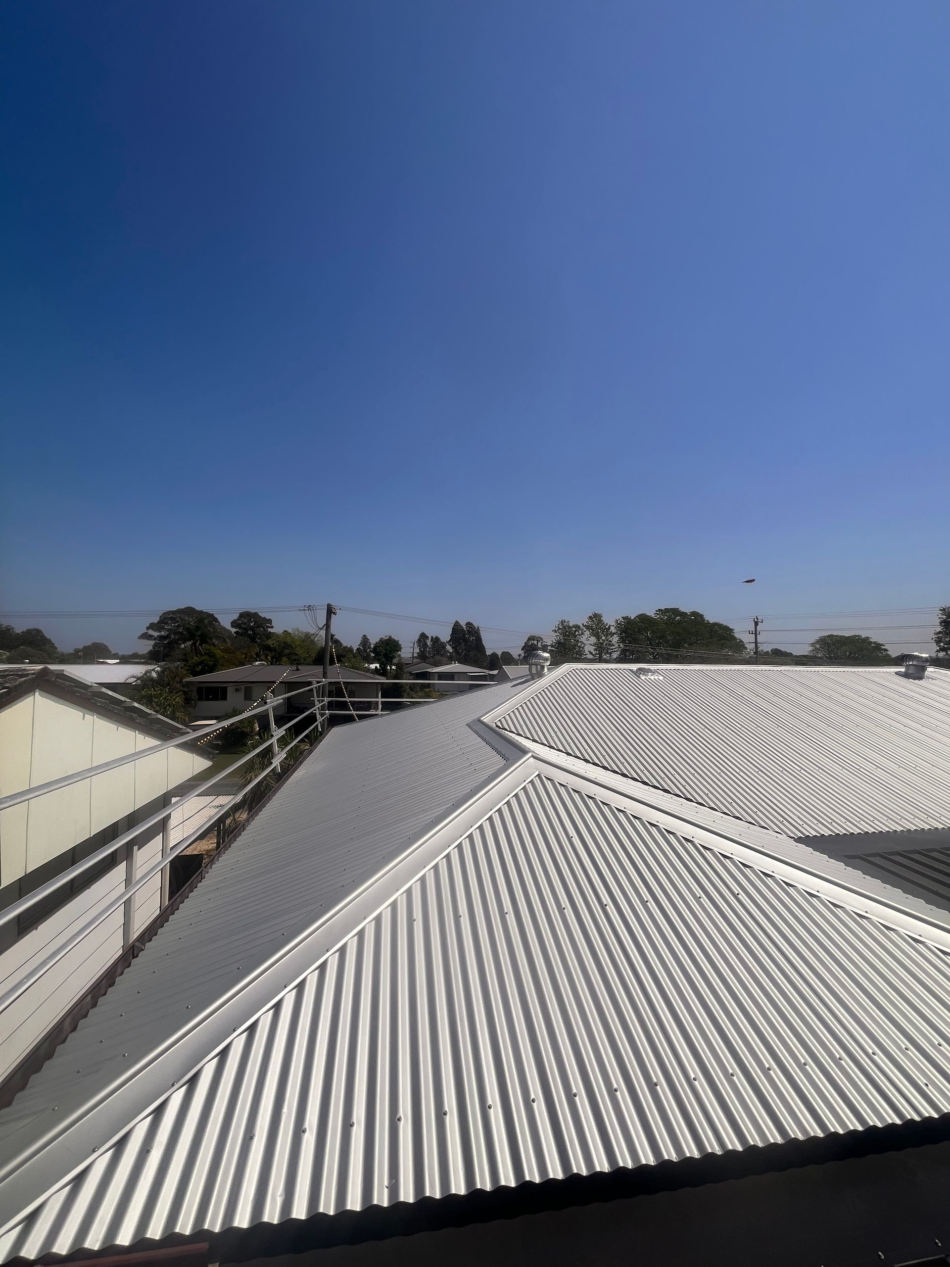 View of a corrugated metal roof under a bright blue sky, trees in the distance.