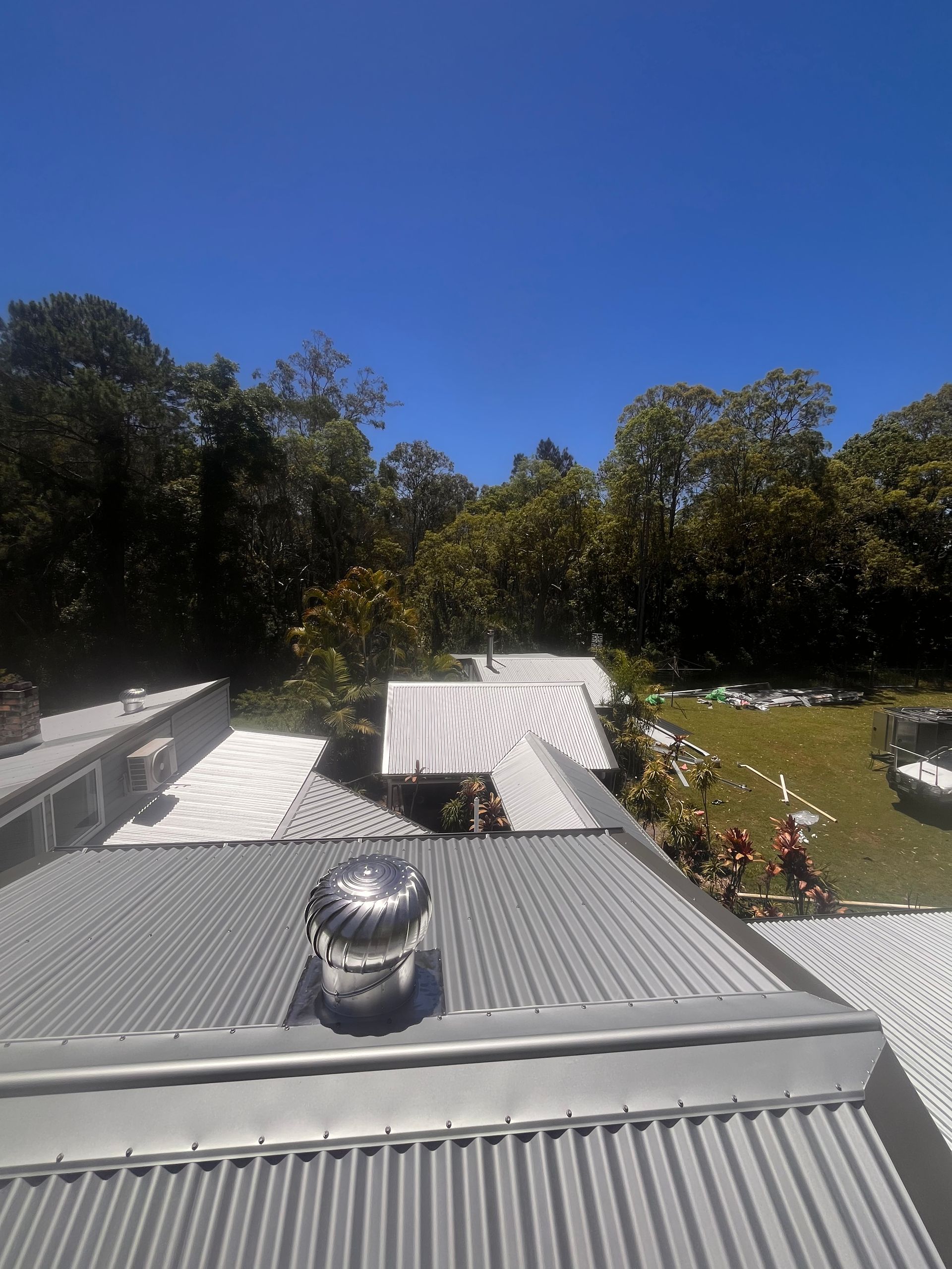Gray metal roofs with vents, trees in background, sunny day.