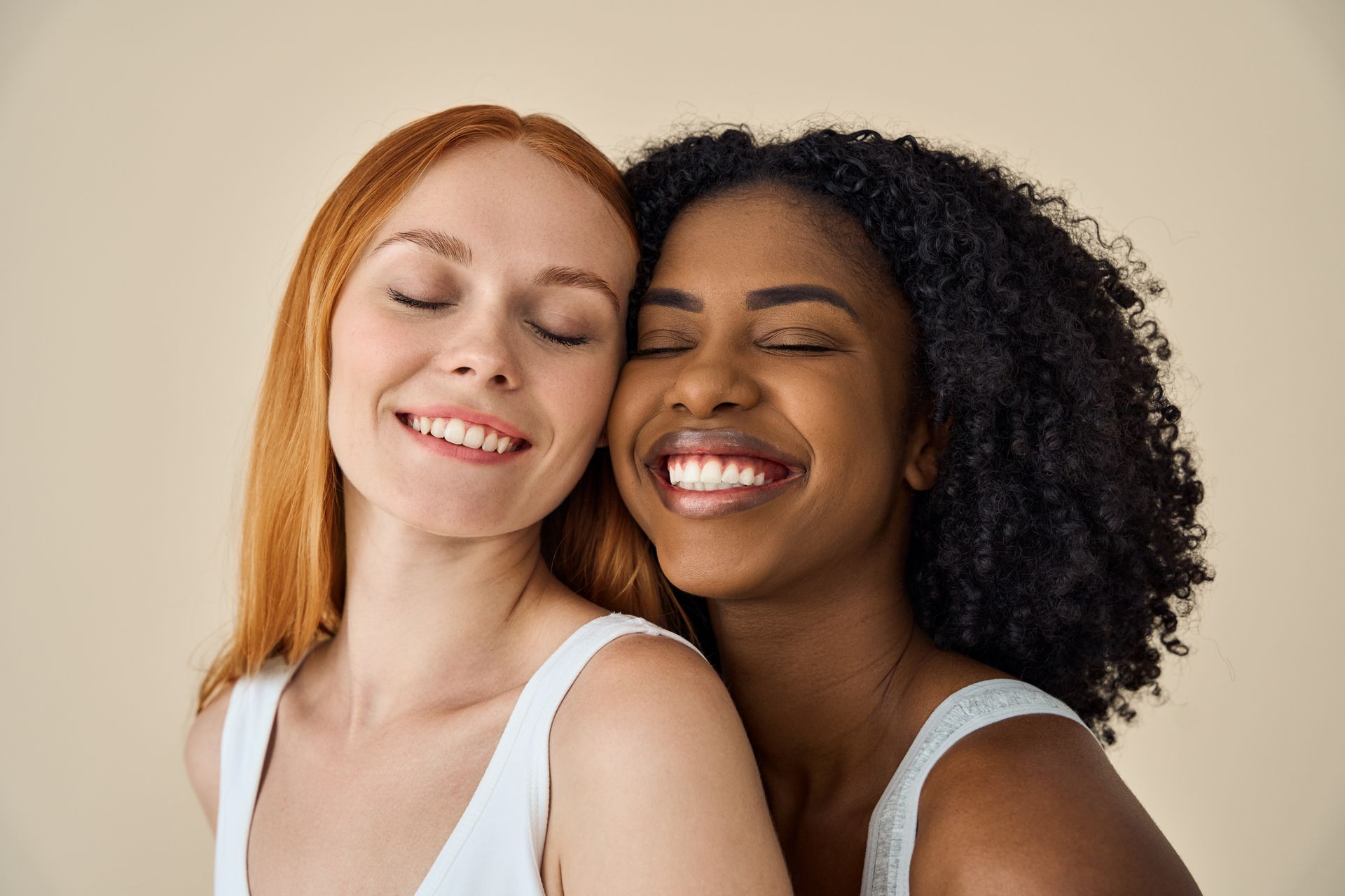 Two women are hugging each other and smiling with their eyes closed.