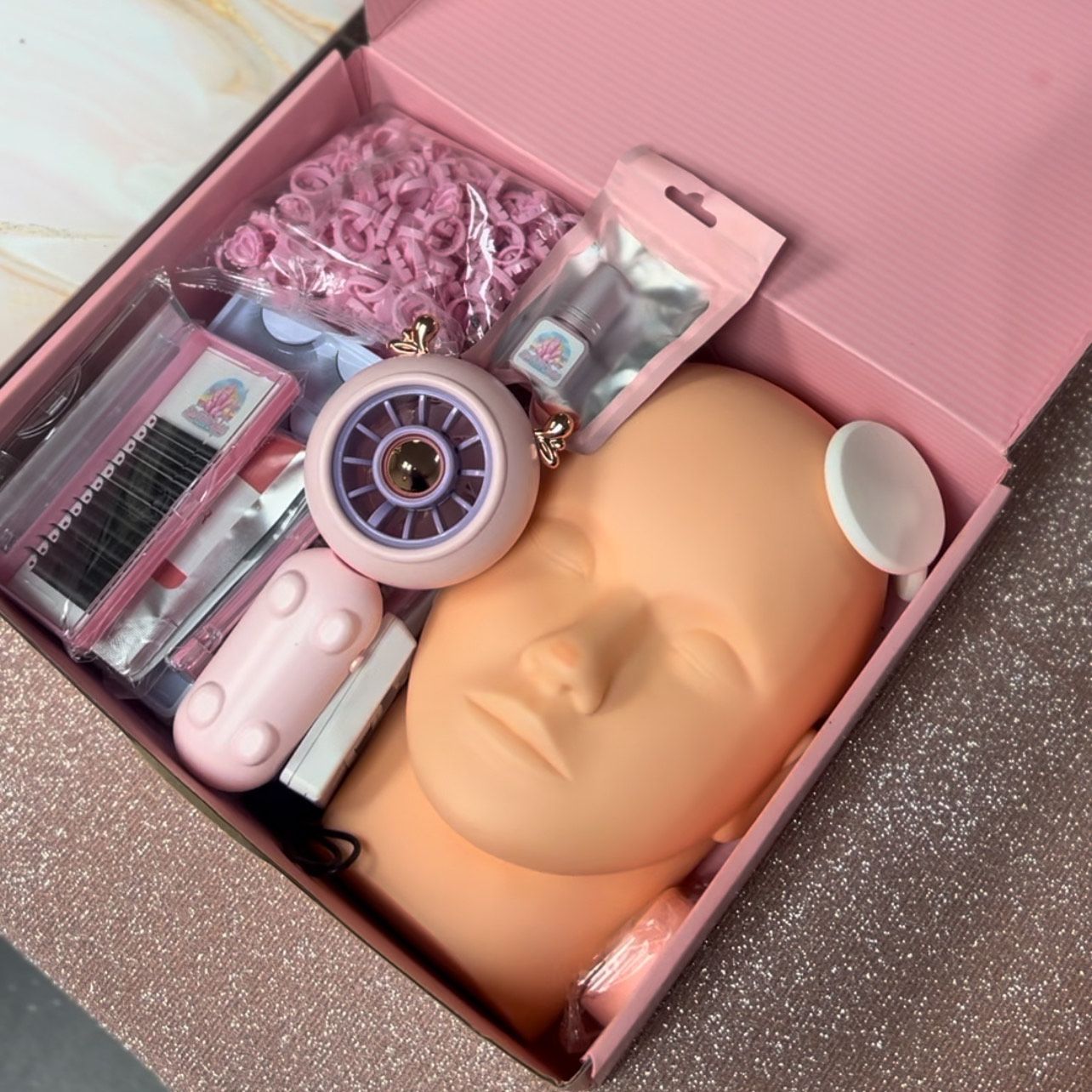 A pink box filled with makeup and a mannequin head.