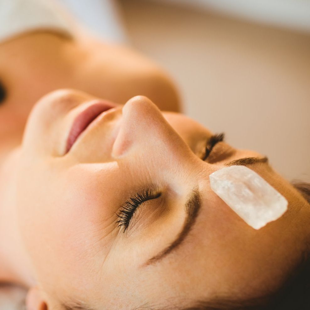 A woman is laying down with a crystal on her forehead.