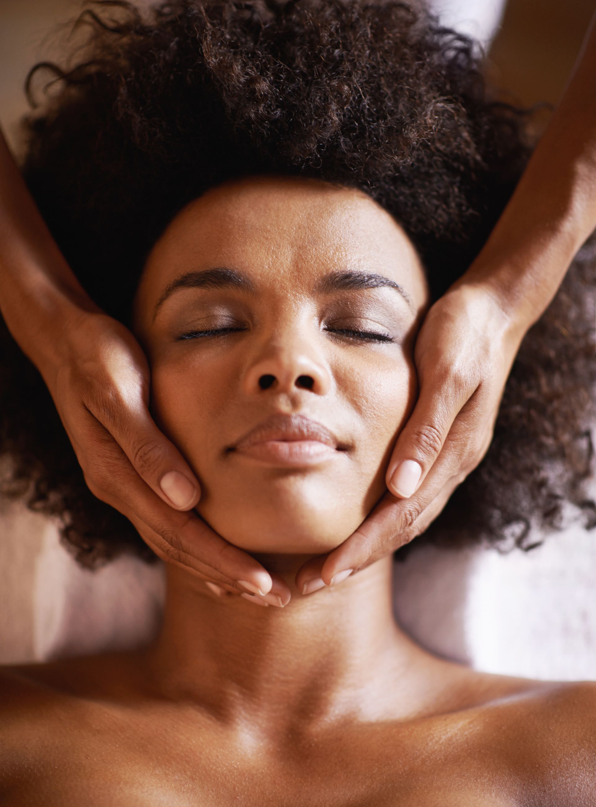 A woman is getting a facial massage with her eyes closed