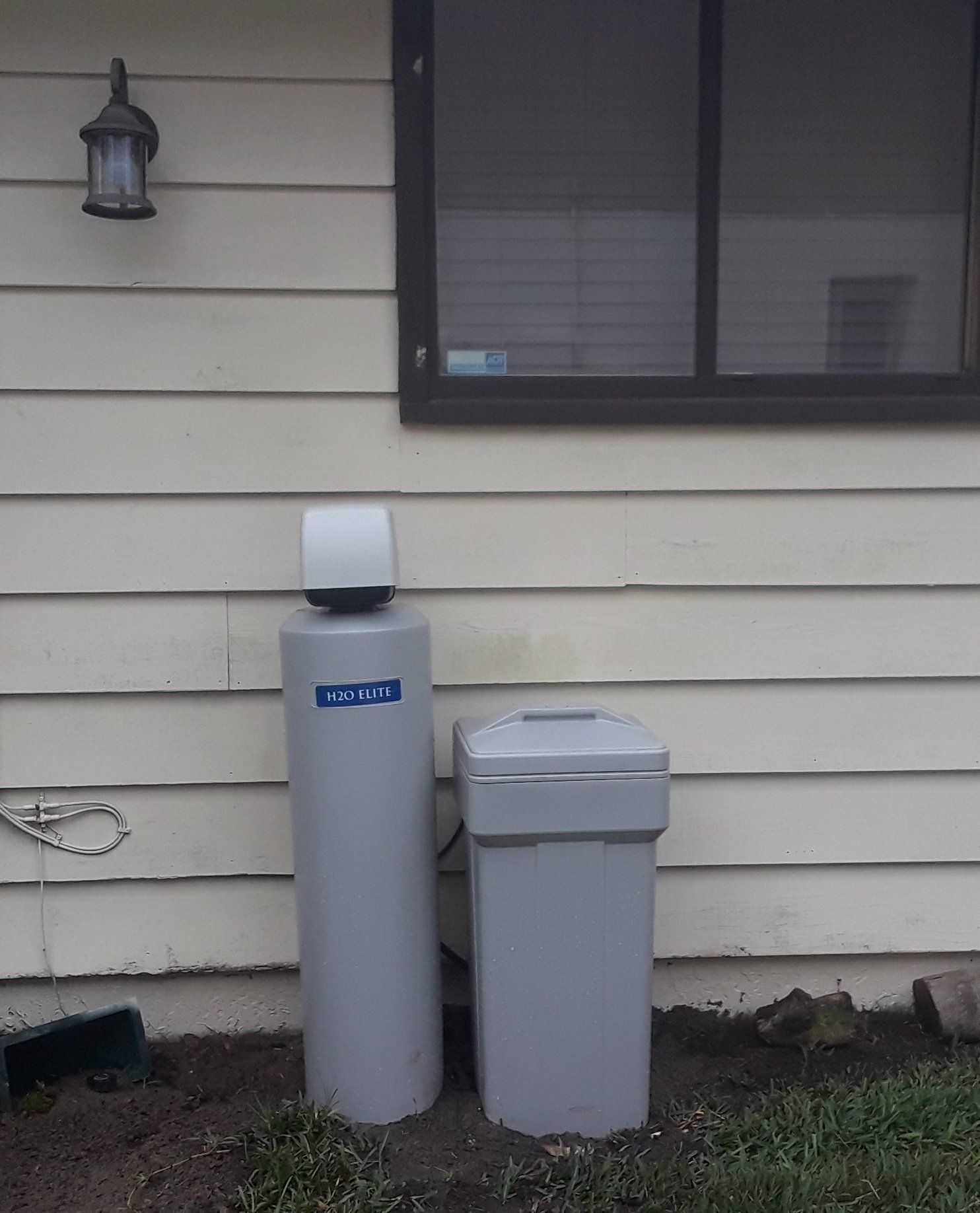 Water softener system next to a house with a window and outdoor light.