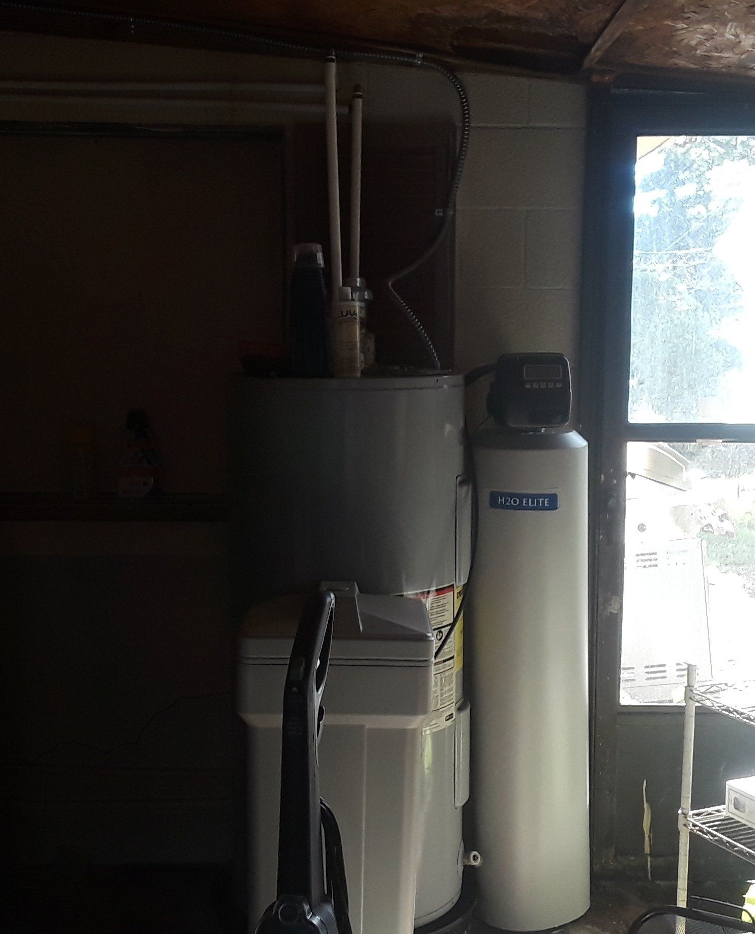 Water heater, water softener, and filter next to a window in a utility room.