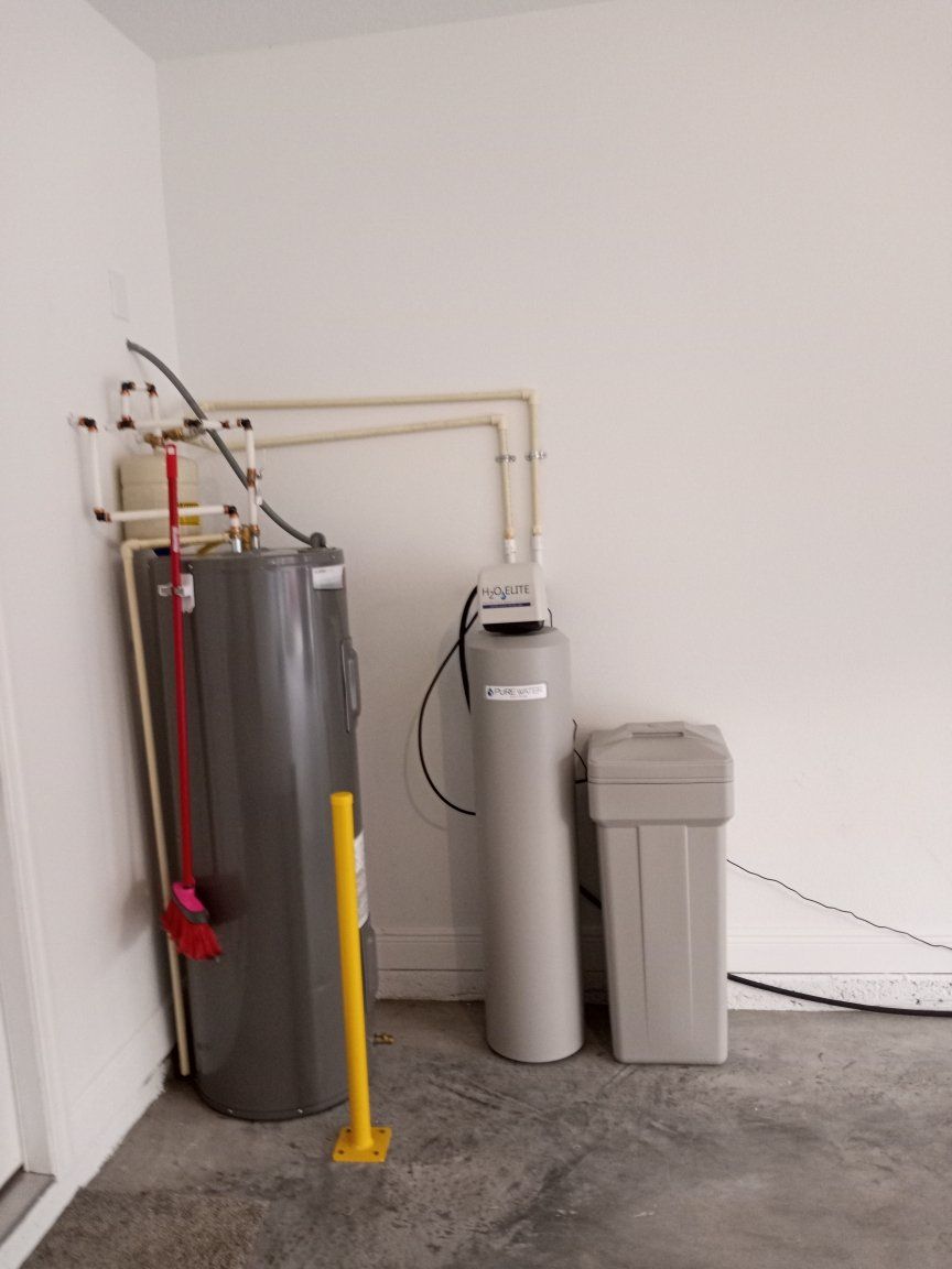 Water heater, filter, and softener in a white-walled garage with concrete floor.