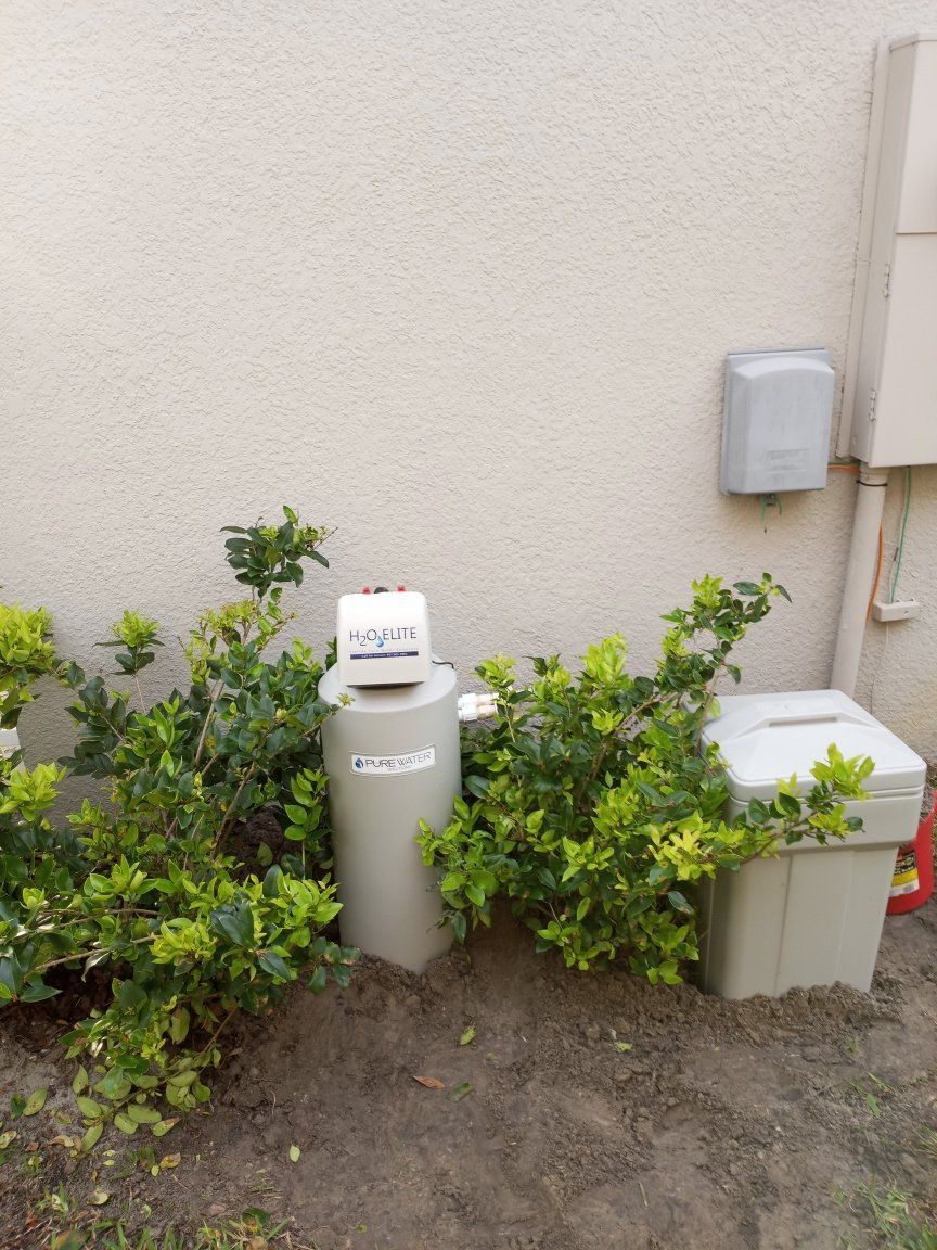 A small, tan septic tank system beside a building, surrounded by green shrubs.